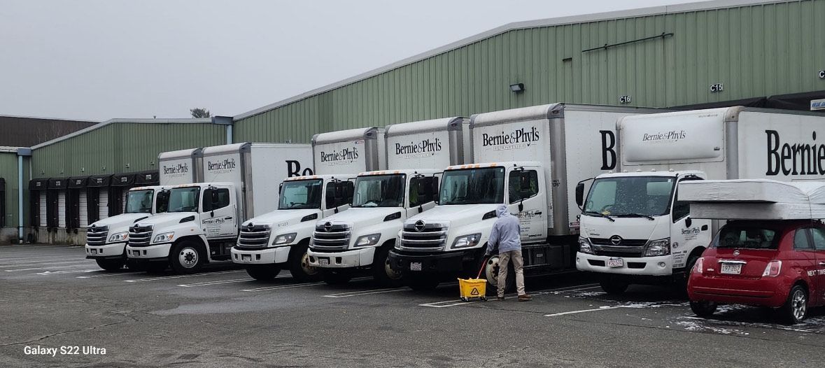 White delivery trucks parked in front of a building. A person is near one truck; a red car is beside.