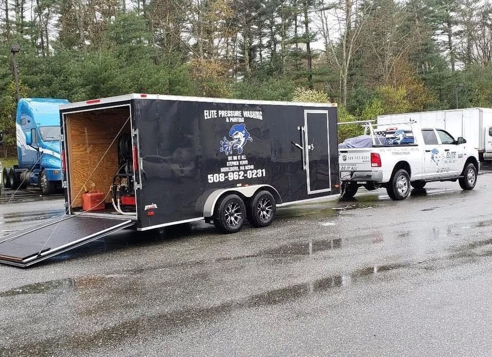 White pickup truck towing a black trailer with open ramp; rainy parking lot.