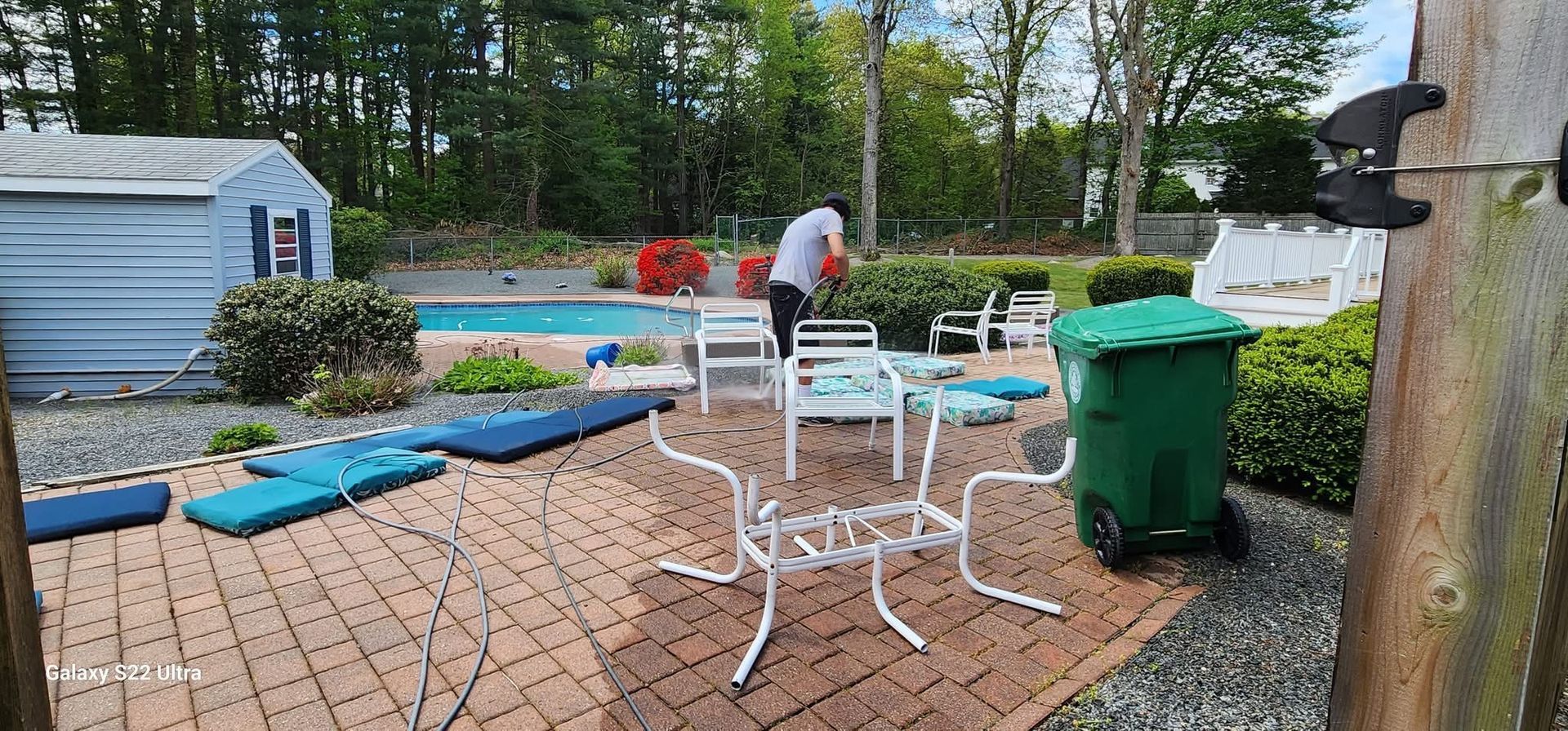 Backyard with pool, patio furniture, green trash can, and person gardening.