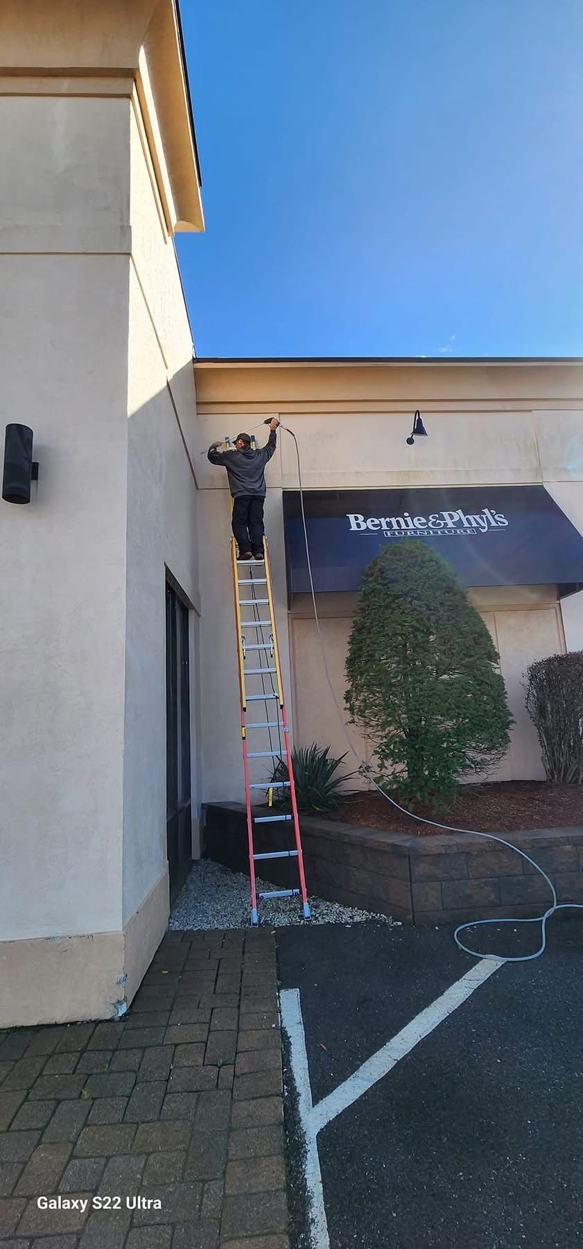 Person on a ladder, installing lights on a restaurant exterior. Sunny day.