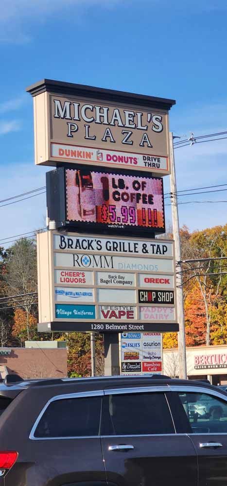 Sign for Michael's Plaza, with a Dunkin' Donuts, Black's Grille & Tap, and other businesses. A dark car is in the foreground.