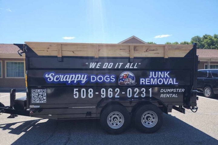 Black Scrappy Dogs Junk Removal trailer with logo and phone number, outdoors on a sunny day.