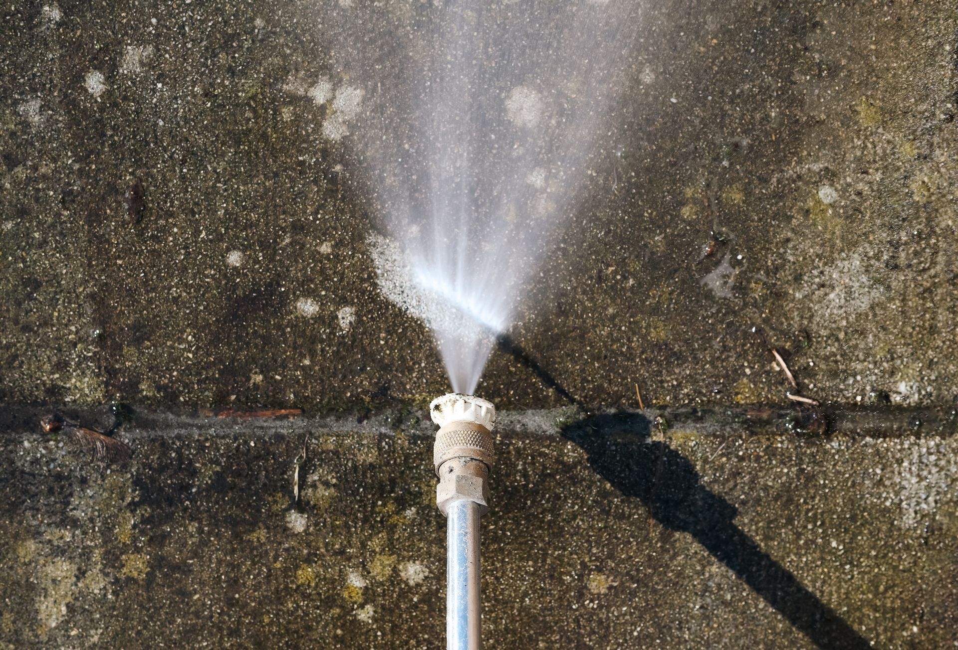 Pressure washer spraying water on a concrete surface, creating a fan-shaped spray.