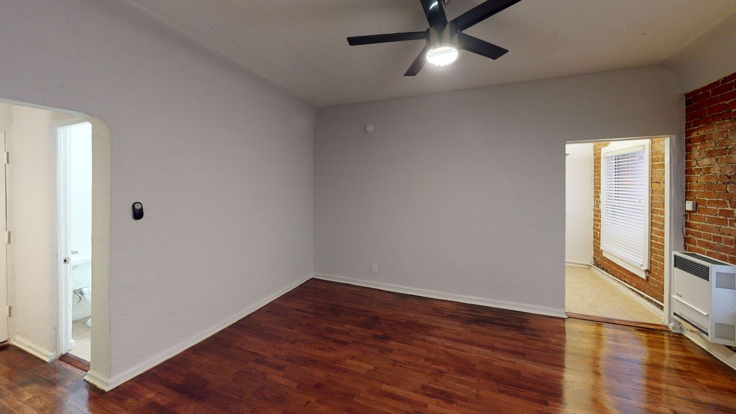 Empty room with dark wood floor, white walls, ceiling fan, and doorways to other rooms.