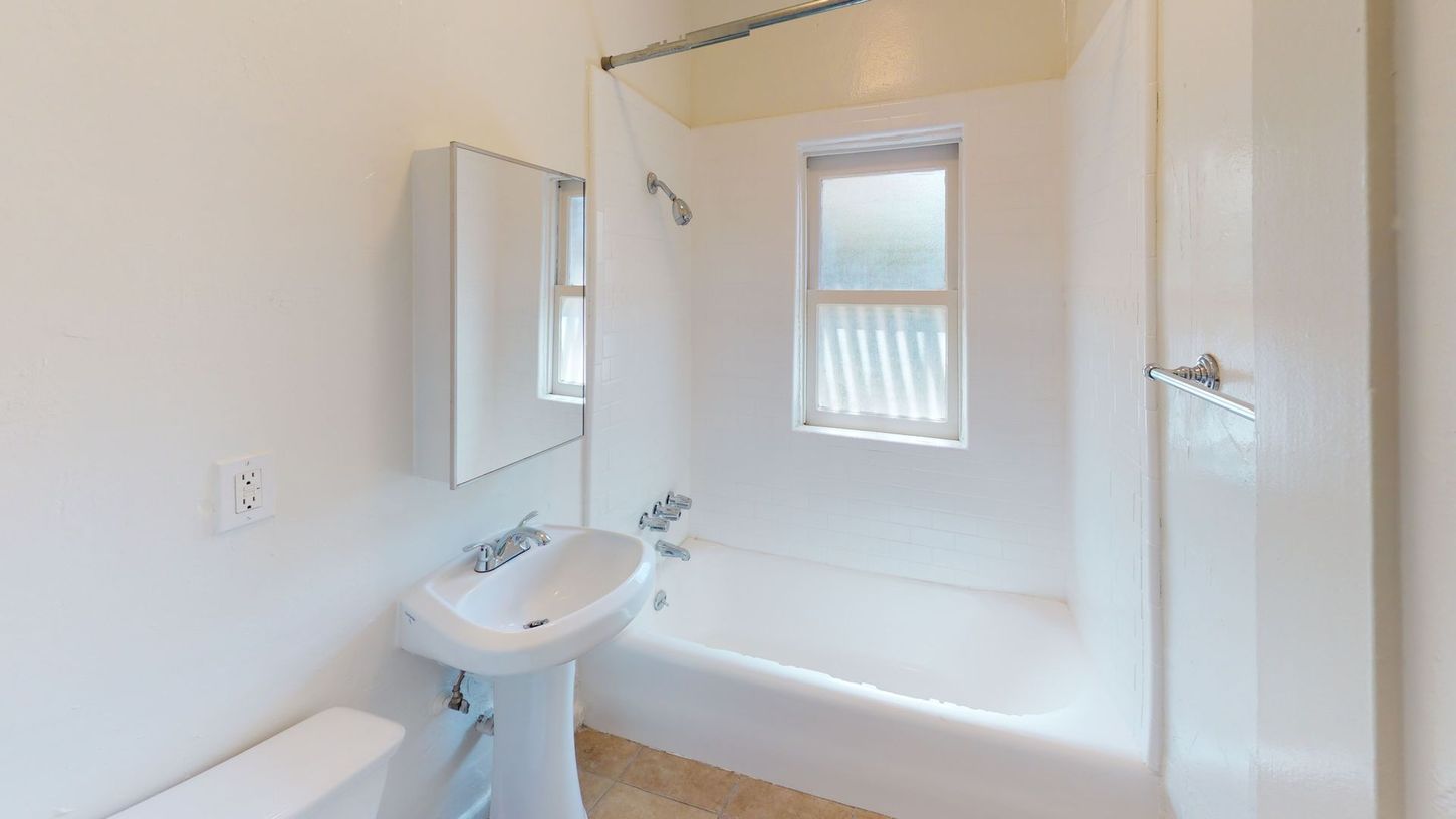 White bathroom with a pedestal sink, bathtub, and a window.
