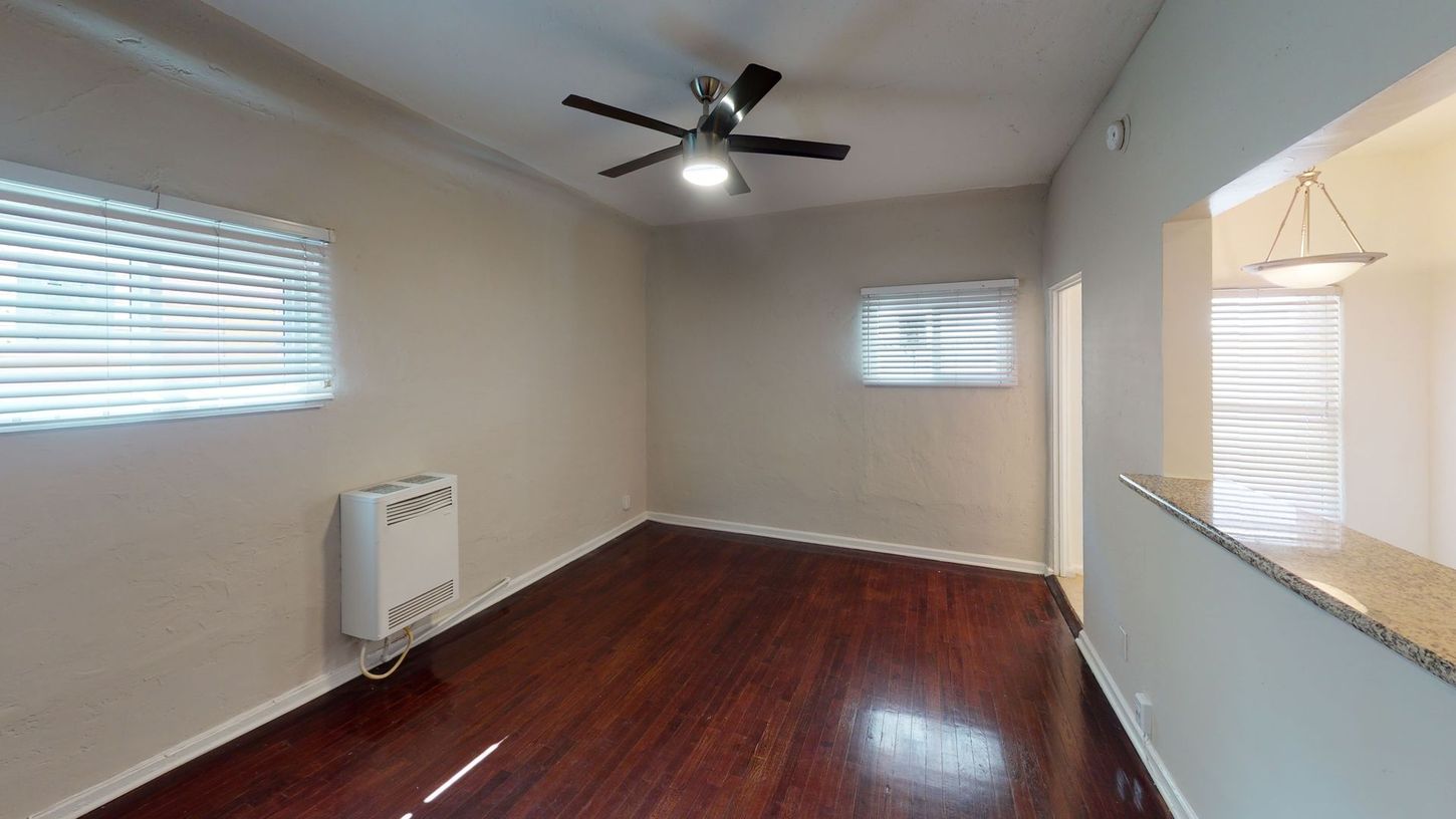 Empty living room with dark hardwood floors, two windows, and a ceiling fan.