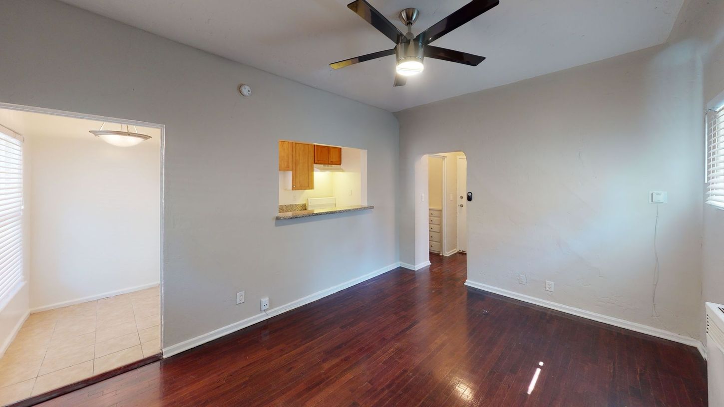 Interior shot of living room with hardwood floors, kitchen pass-through, and ceiling fan.