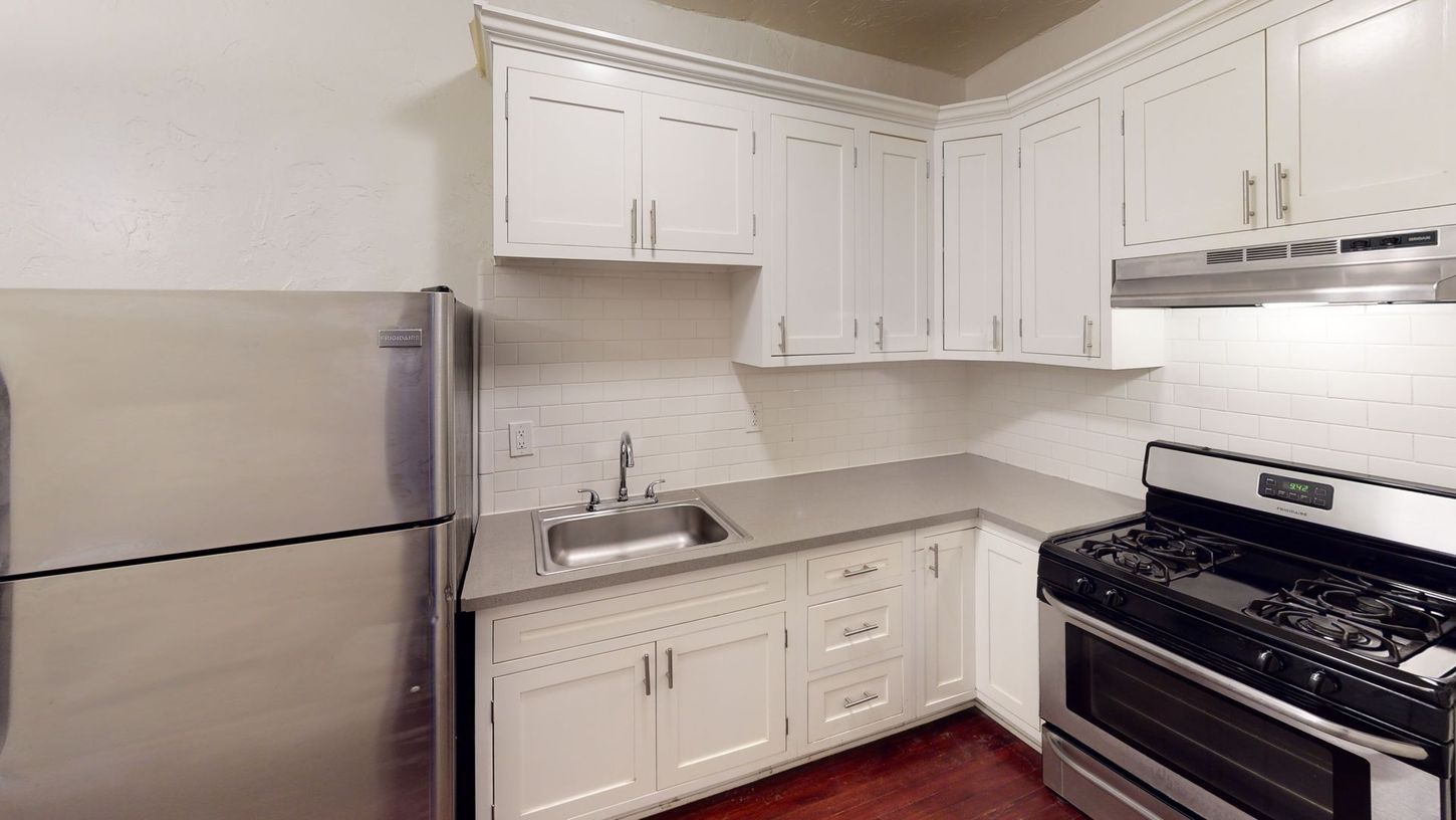 Small white kitchen with stainless steel appliances, dark wood floor, and light countertops.