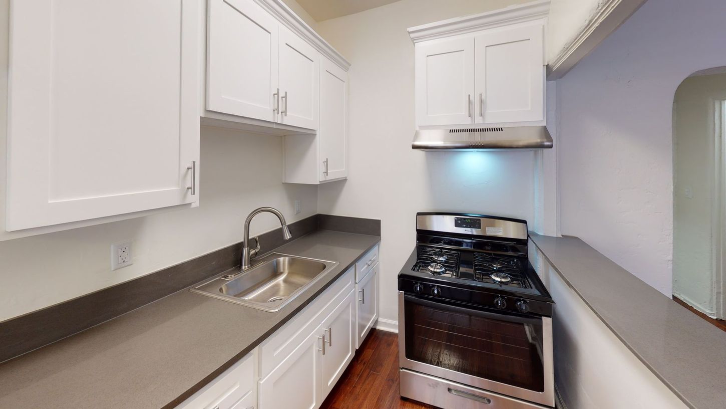 Small kitchen with white cabinets, dark countertops, stainless steel appliances, and hardwood floors.