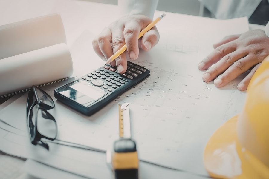 Contractor using a calculator over blueprints with a hard hat and tape measure on the desk