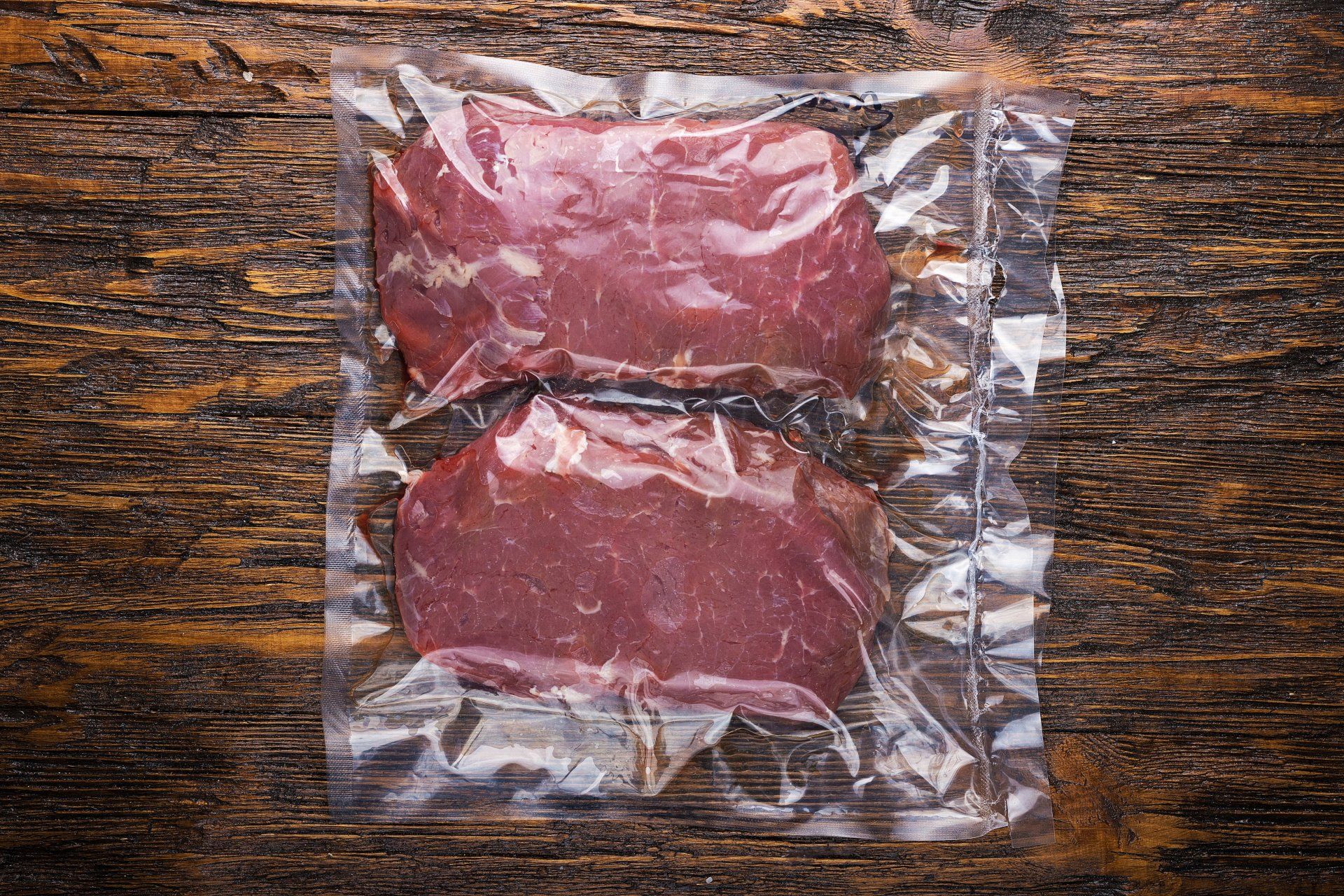 Two steaks in a plastic bag on a wooden table.