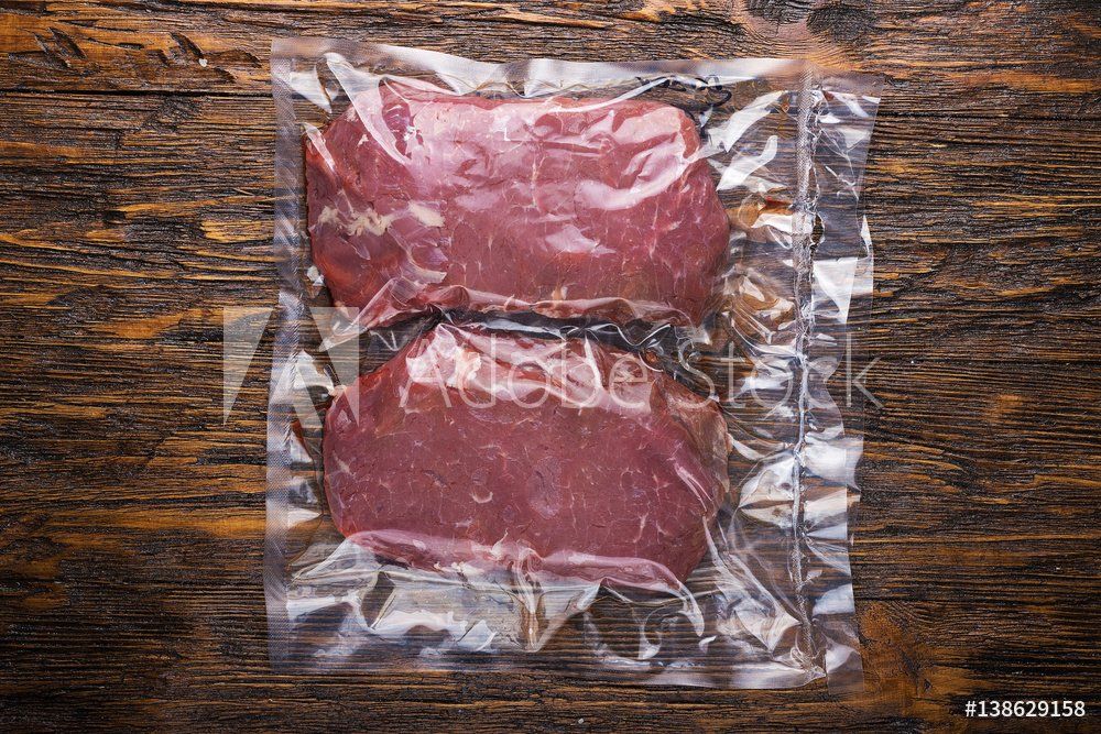 Two steaks in a plastic bag on a wooden table.