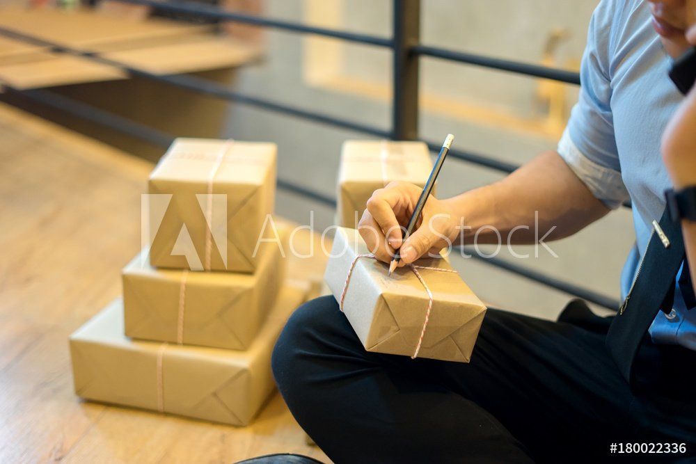 A man is sitting on the floor writing on a box.