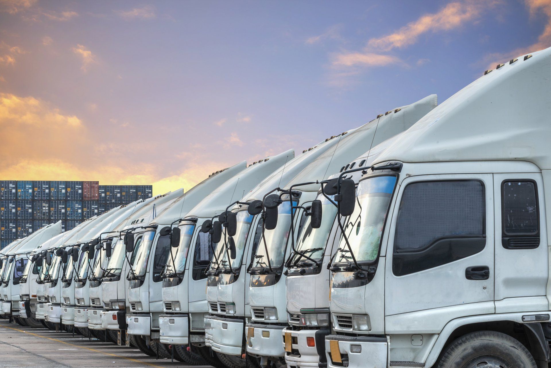 A row of white trucks are parked next to each other in a parking lot.