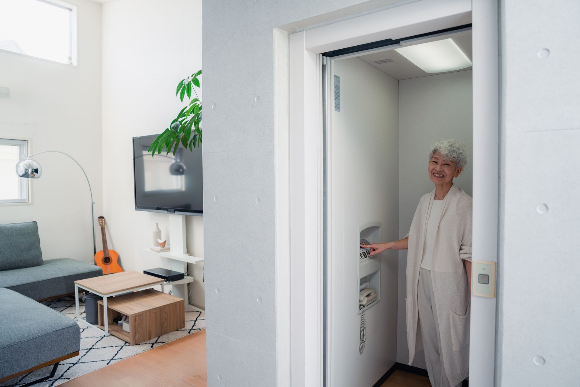Woman in white clothing operating an elevator in a modern home with a living room visible.