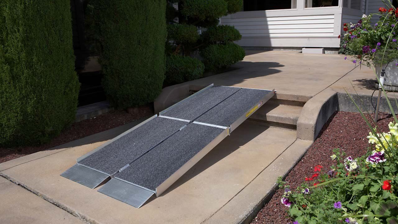Aluminum ramp over a set of steps leading to a house entrance, flanked by bushes and flowers.