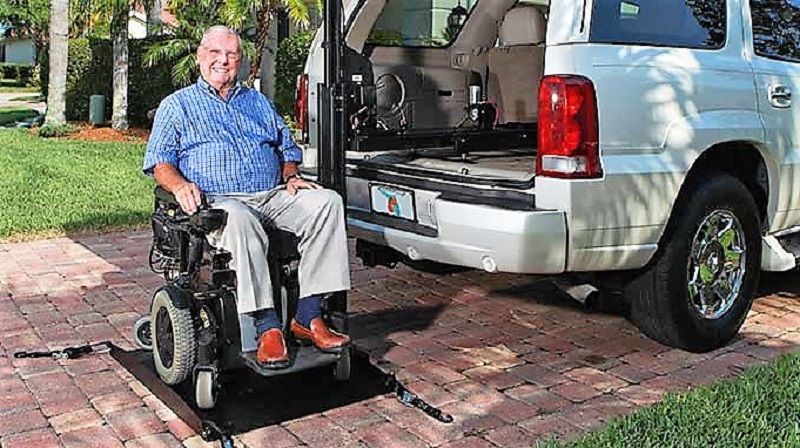 Man in wheelchair using ramp to enter accessible SUV in a driveway.