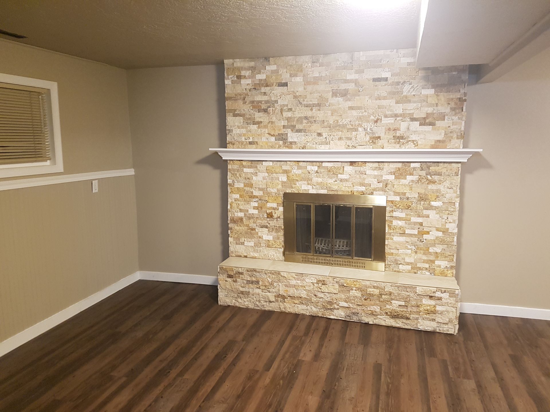 Fireplace with gold trim and stone surround in a tan-walled room with wood-look flooring.