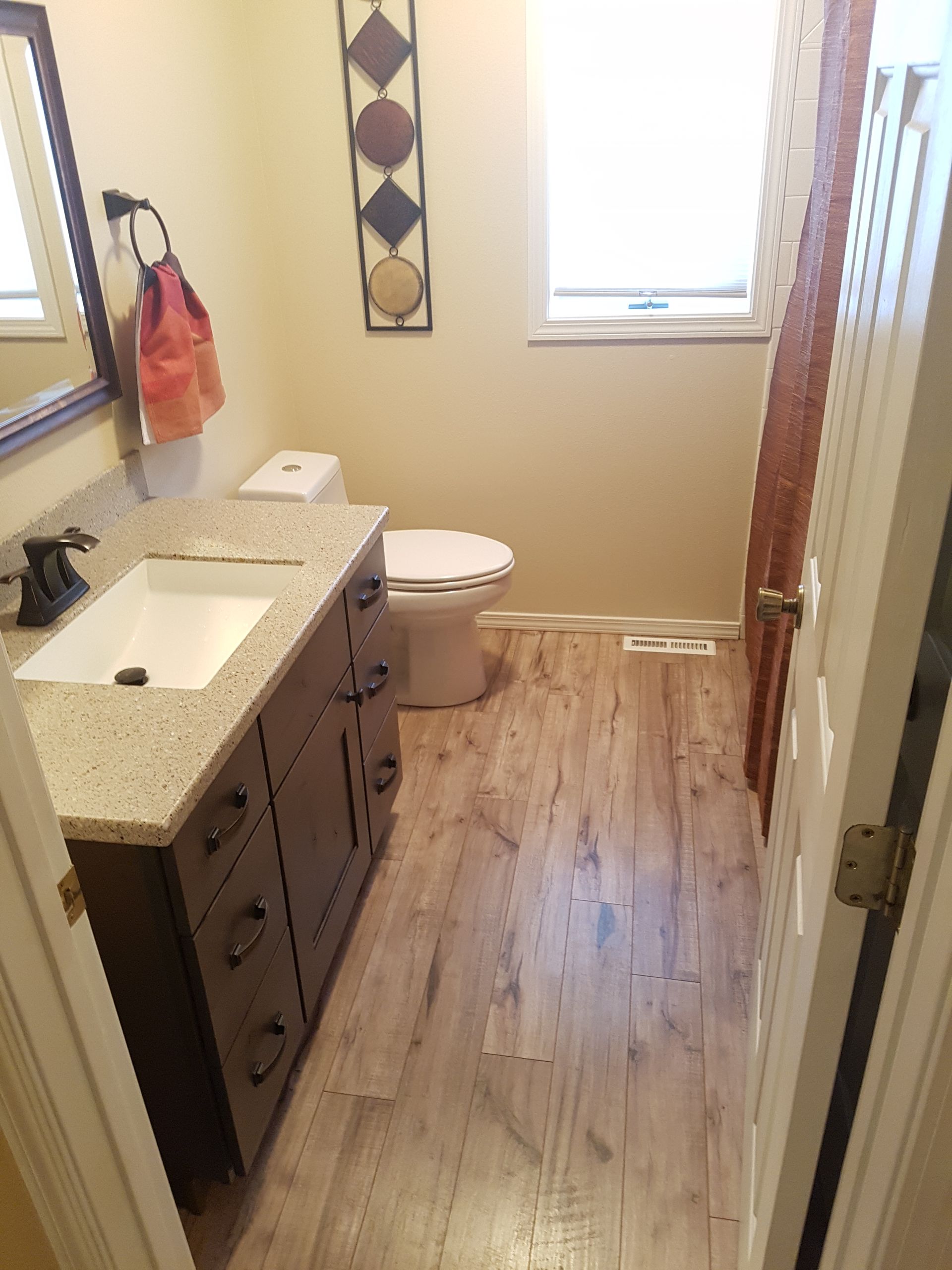 Bathroom with dark brown vanity, toilet, wood-look flooring, and decorative wall art.