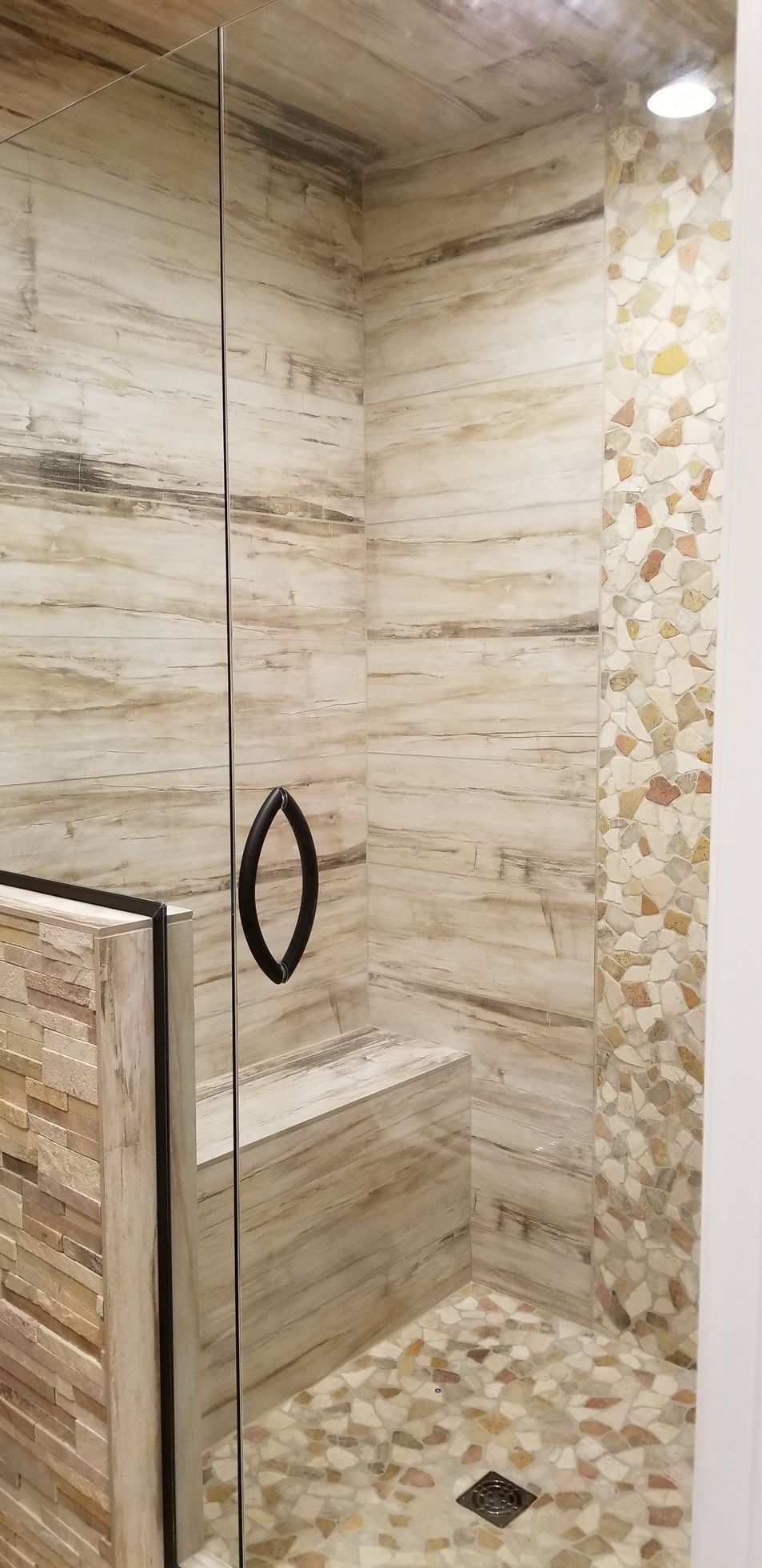 Shower stall with pebble floor, textured wall and glass door with dark handle.