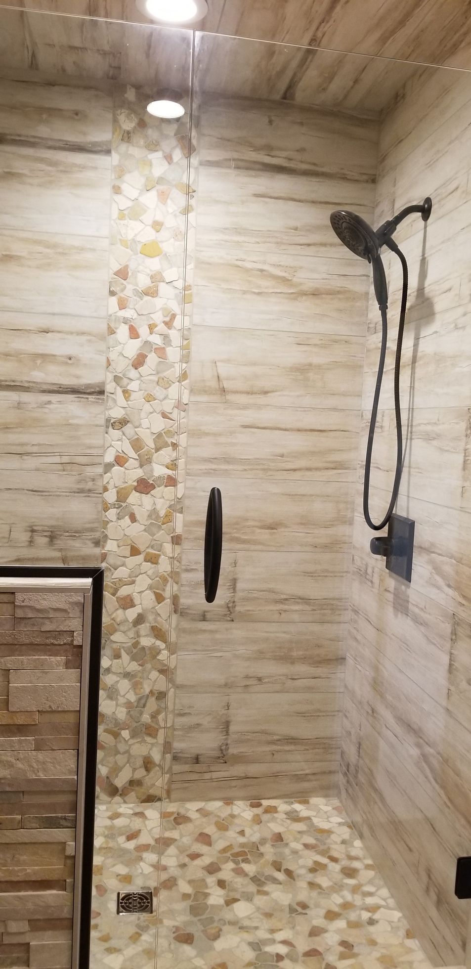 Bathroom interior with a pebble-stone shower floor, stone tile walls, and dark fixtures.