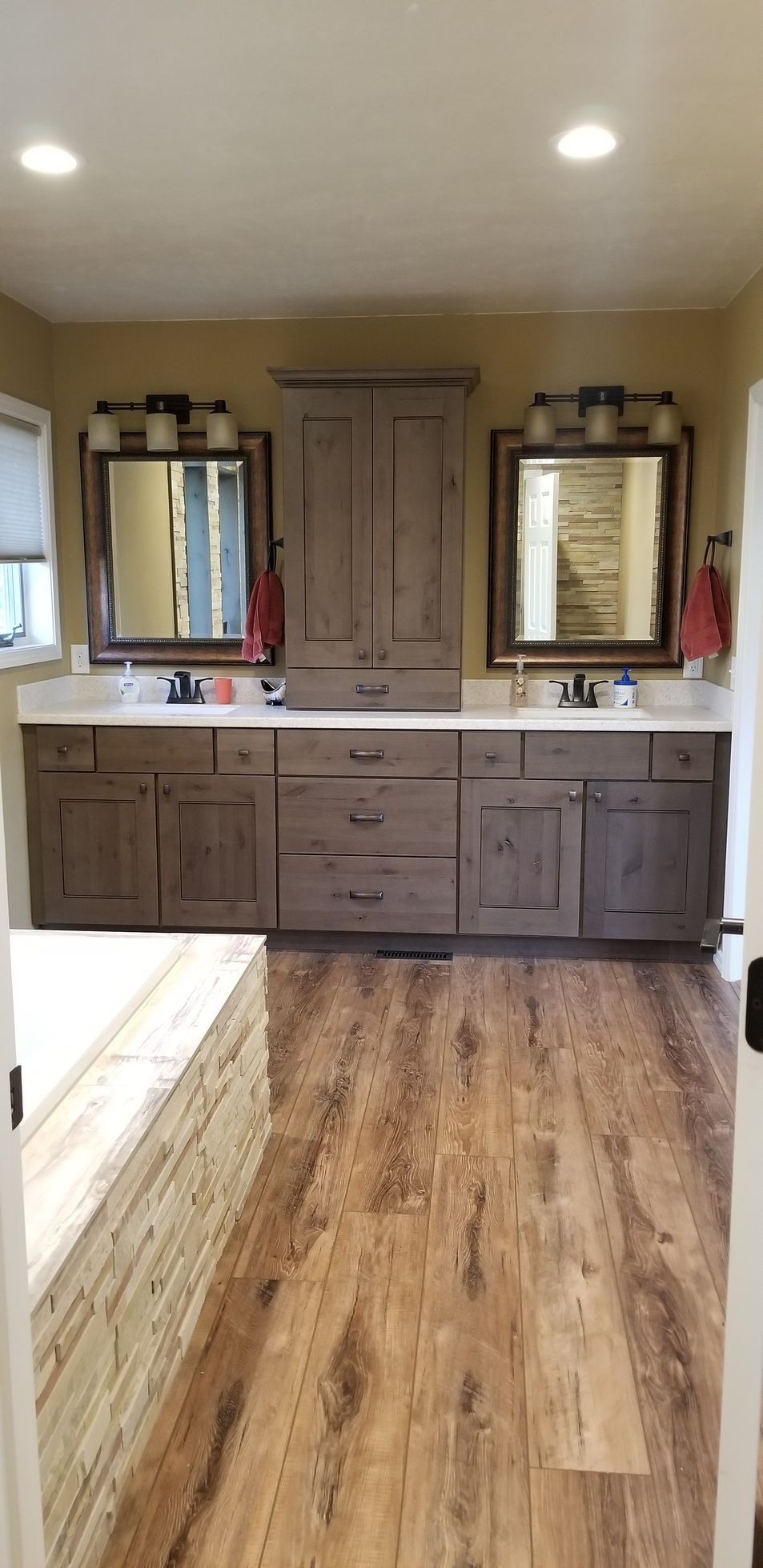 Bathroom with wood flooring, double vanity, mirrors, and central cabinet.