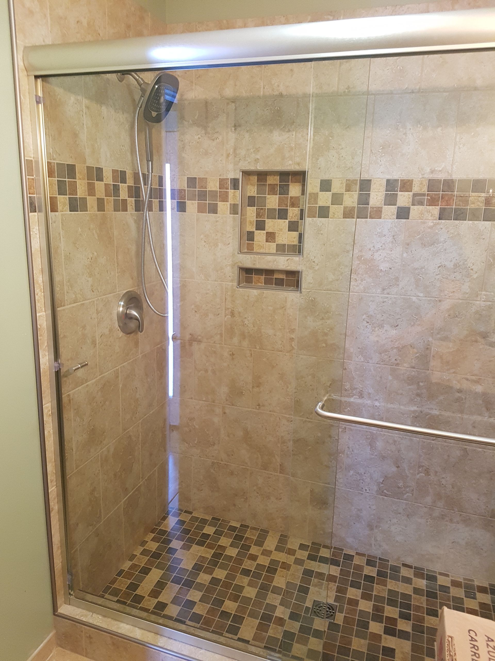 Shower with glass doors, tiled walls, built-in shelf, and pebble floor.
