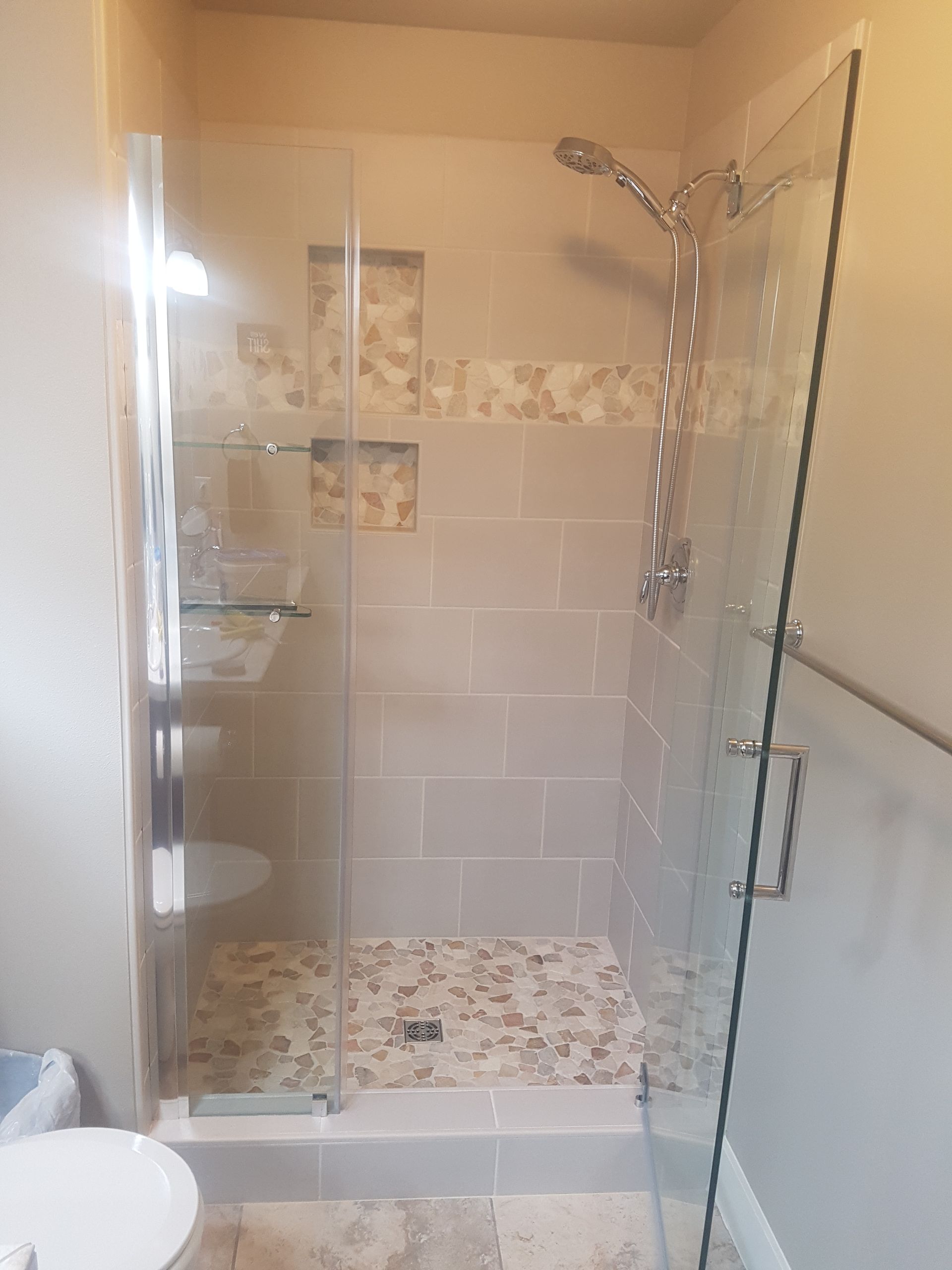 Glass-enclosed shower with tiled walls and floor, chrome fixtures, and built-in shelves.