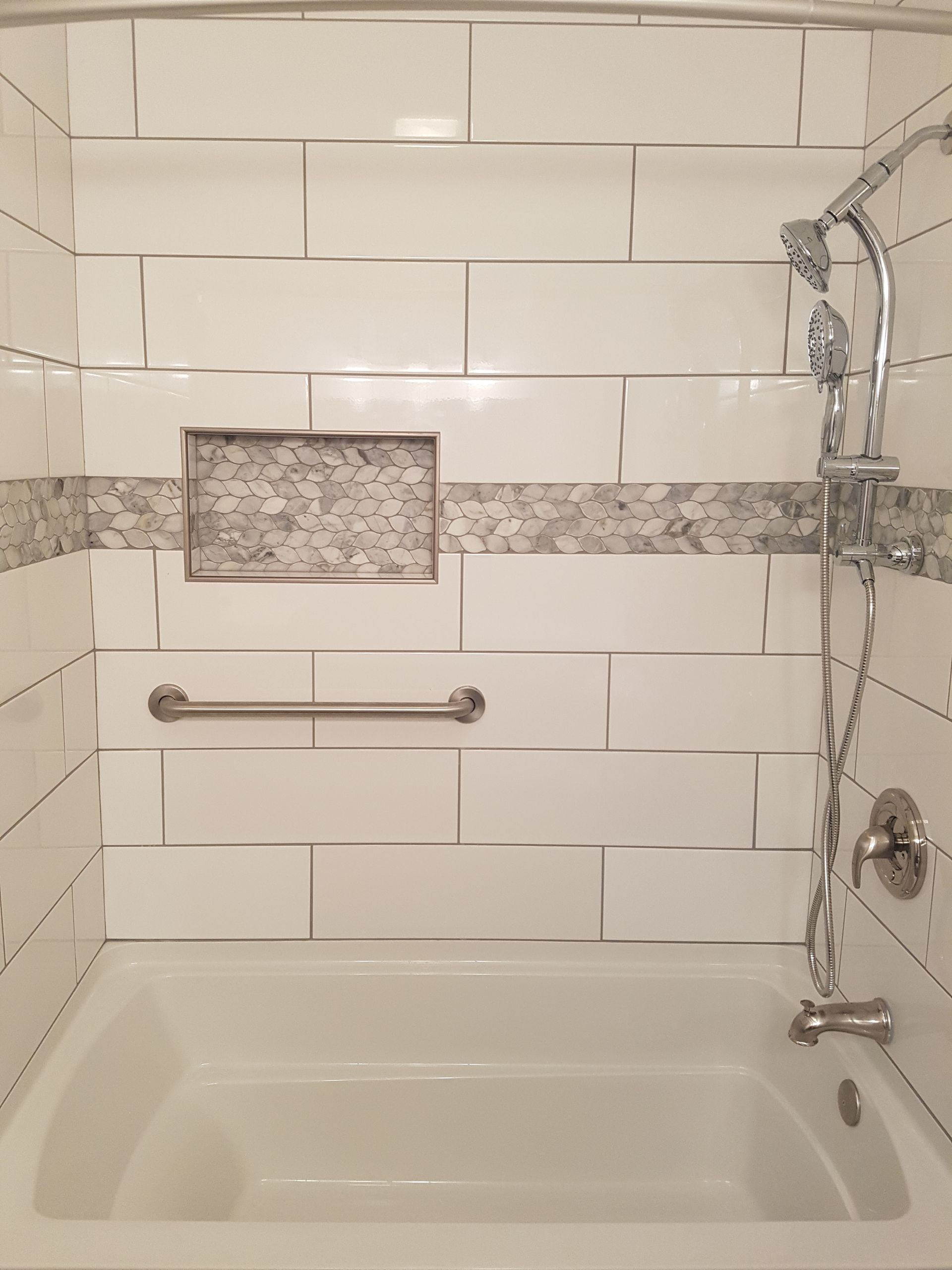 White tiled shower with a built-in shelf, grab bar, and shower fixtures.