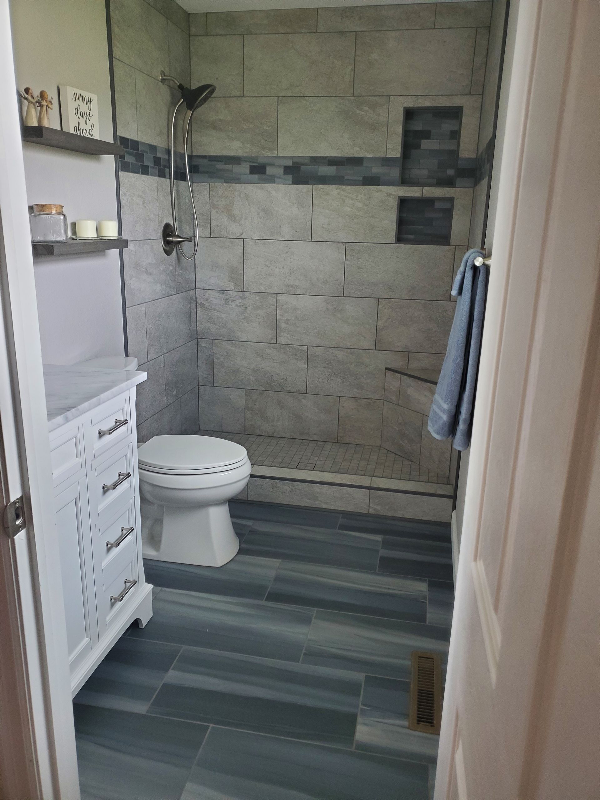 Bathroom with gray tiled shower, blue floor, white vanity, and toilet.