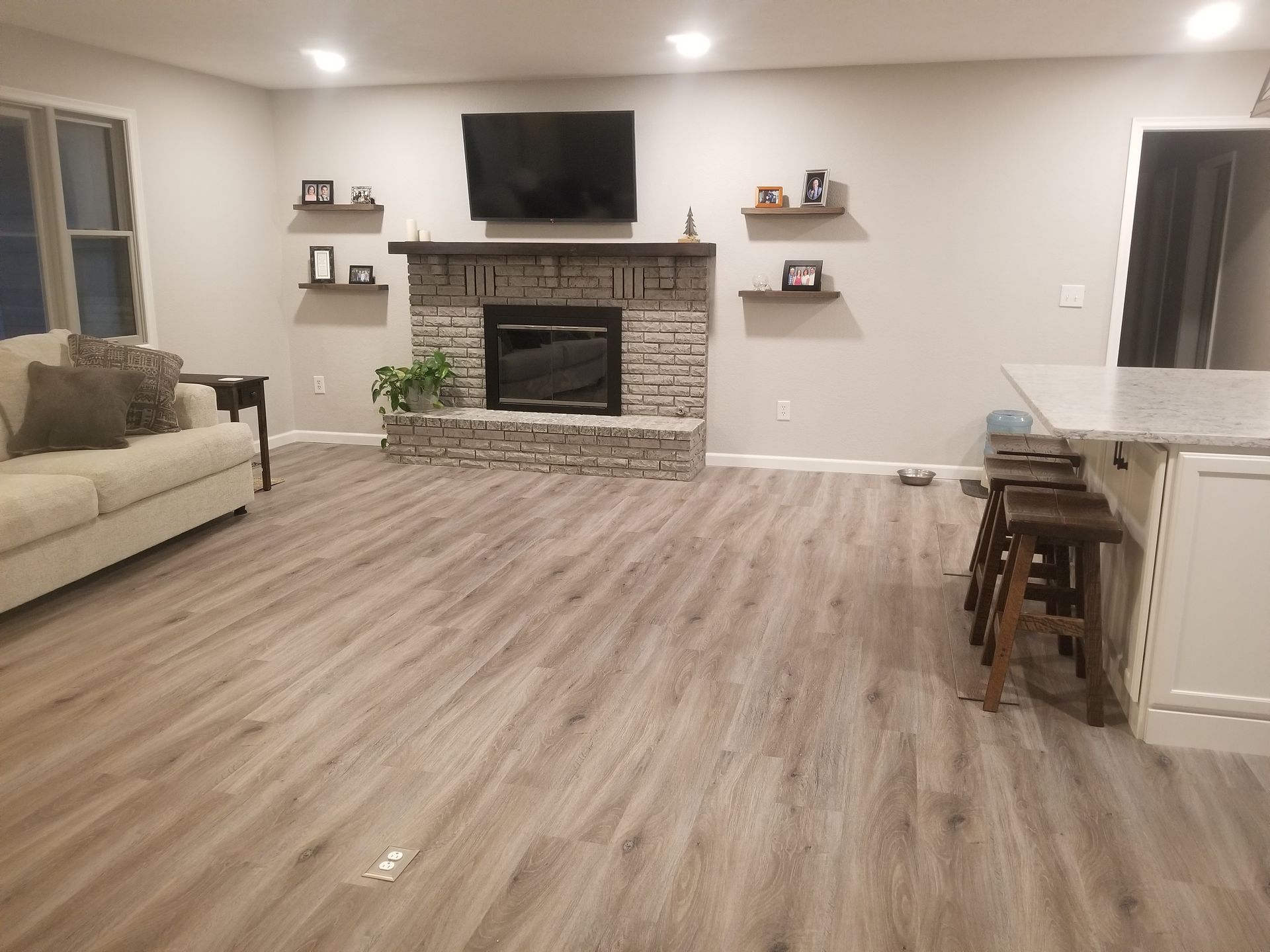 Living room with light gray walls, fireplace, TV, shelves, and wood-look flooring.