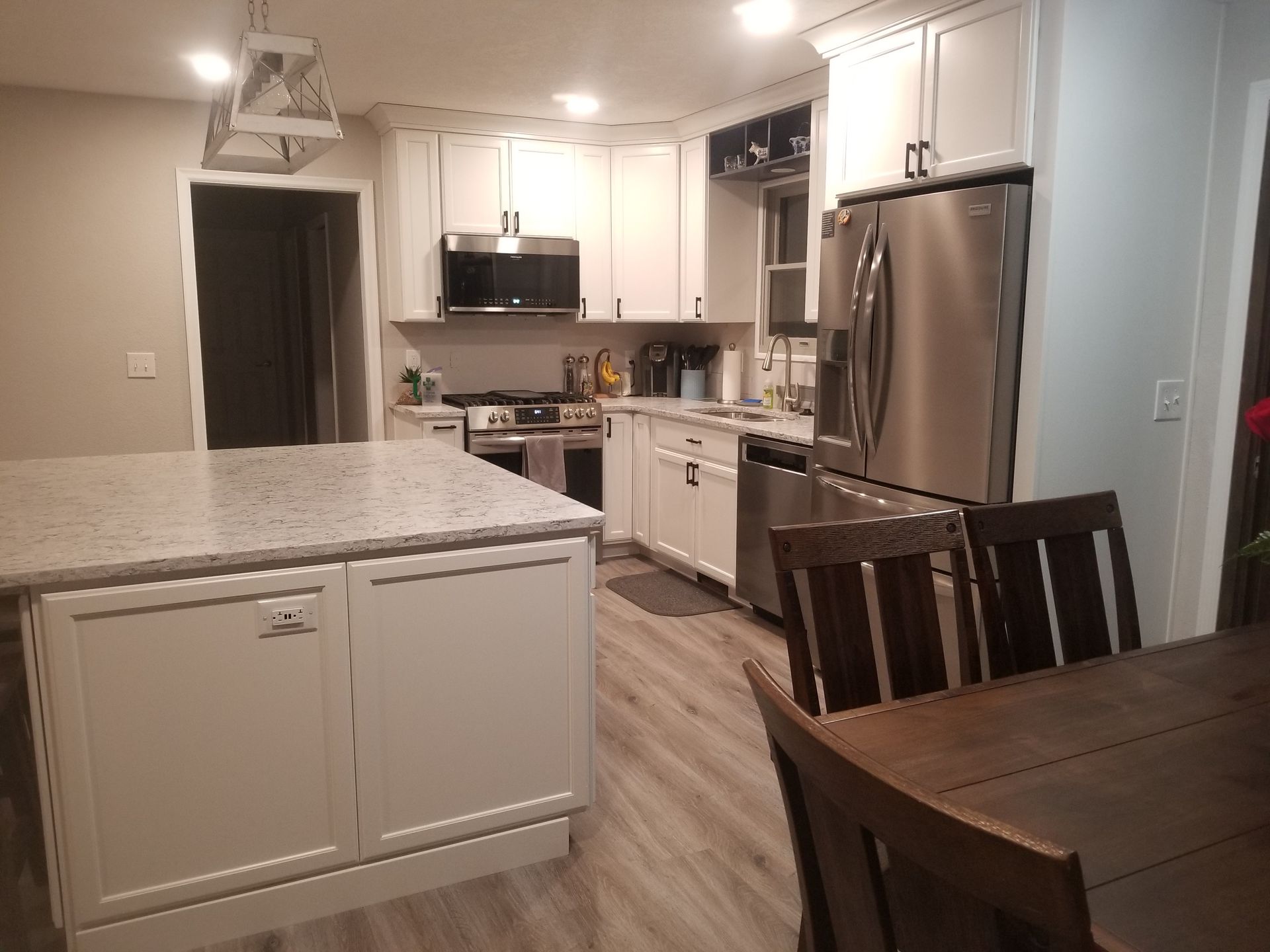 White kitchen with stainless steel appliances, an island, and wood dining table.