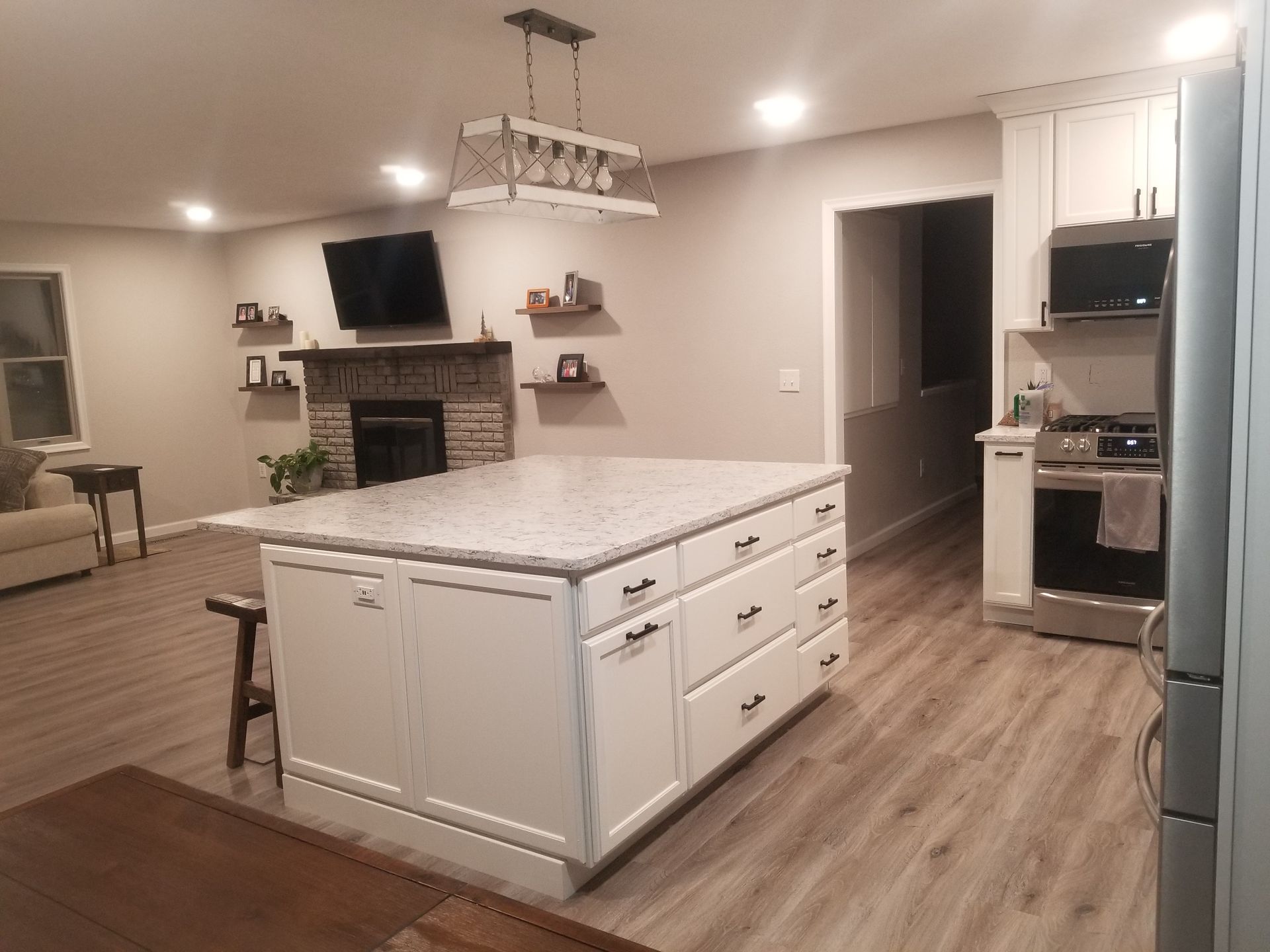 Modern kitchen with white cabinets, island, and granite countertop. Living area with fireplace in the background.