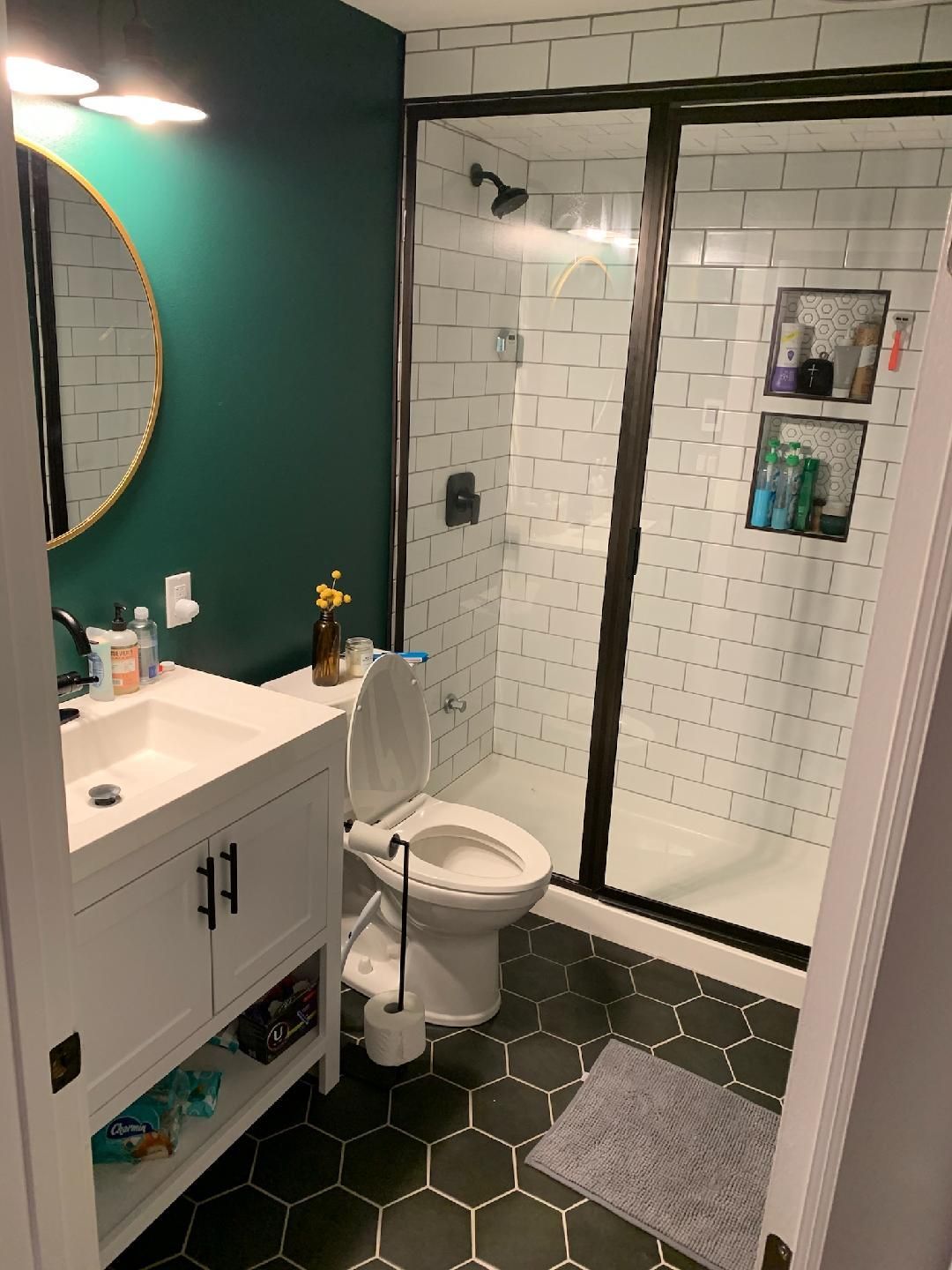 Bathroom with white vanity, emerald wall, black hexagon floor, and a glass shower.