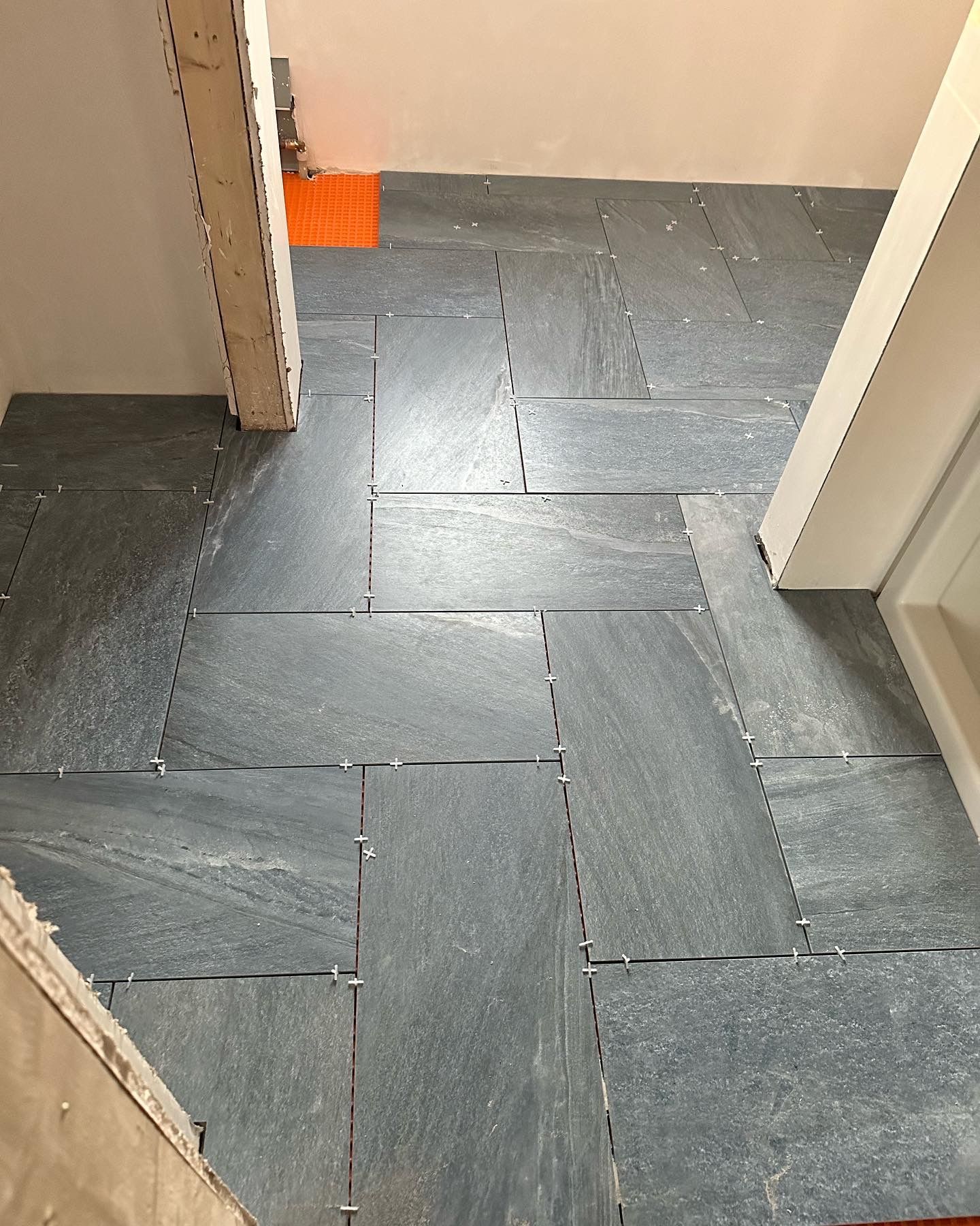 Newly installed gray rectangular floor tiles with spacers in hallway.