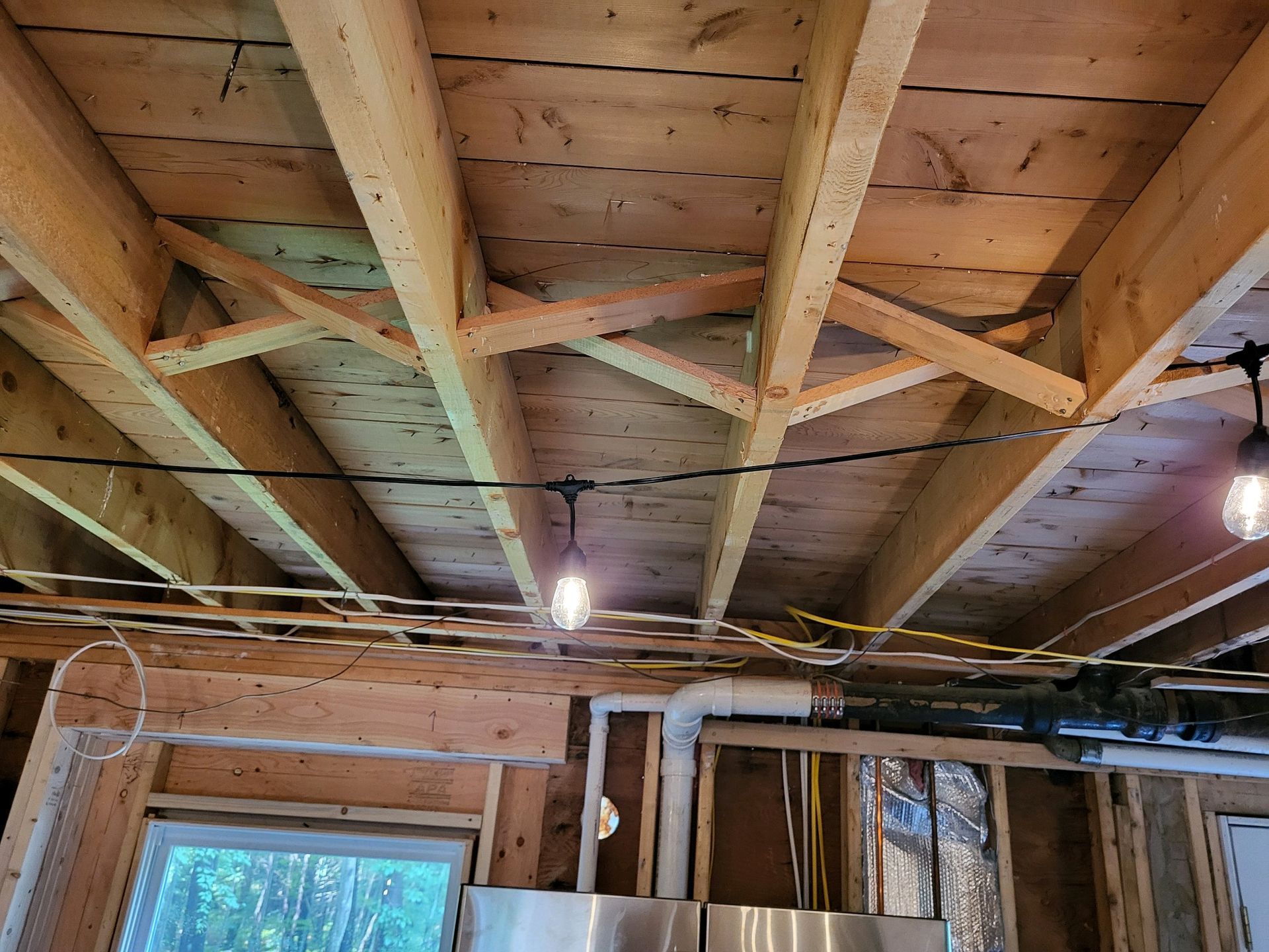 Wooden ceiling framing with X-shaped bracing and exposed electrical wiring in a partially built room.