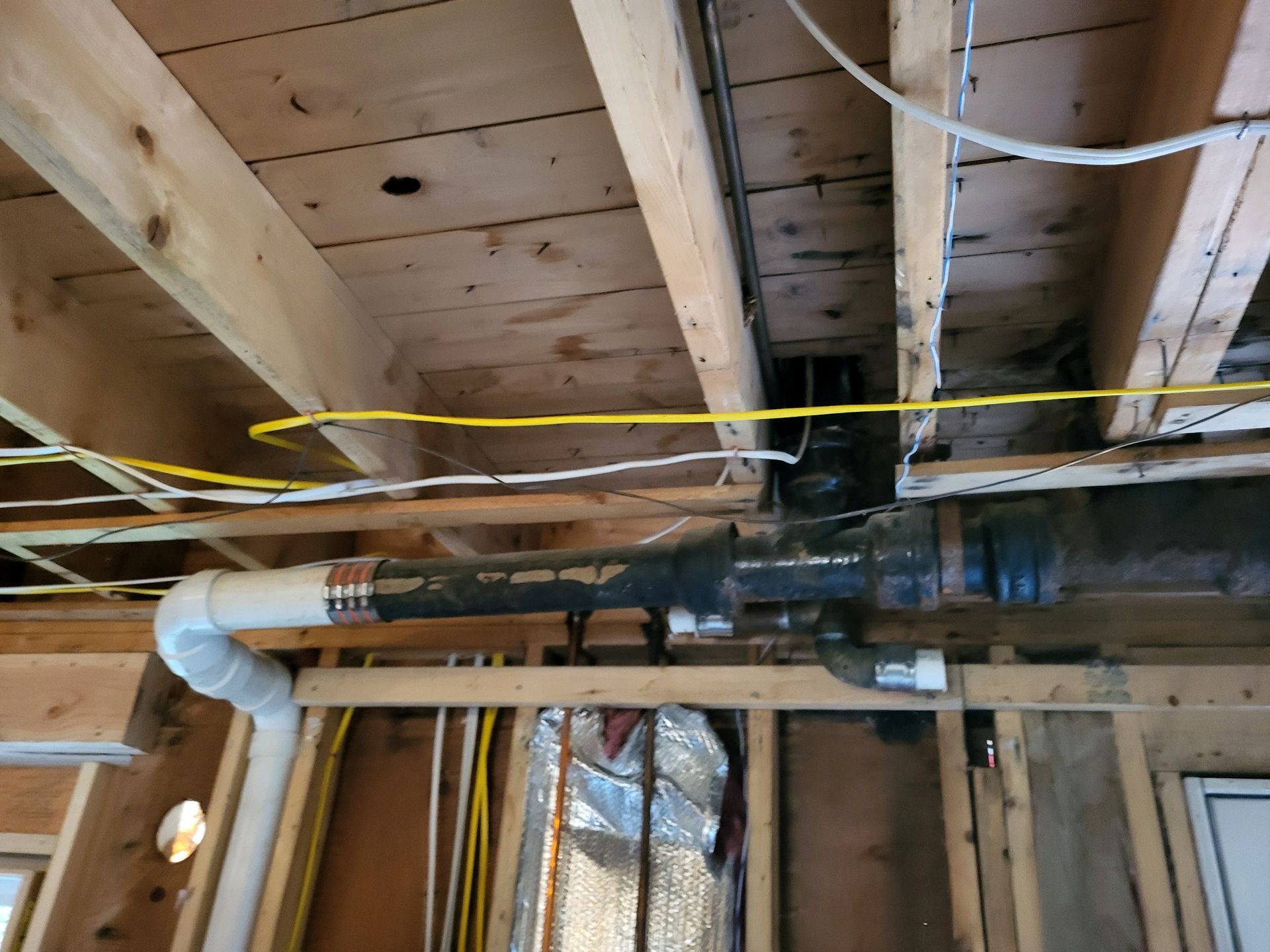 Plumbing pipes and electrical wiring in a wooden ceiling. Black, white, and yellow cables.