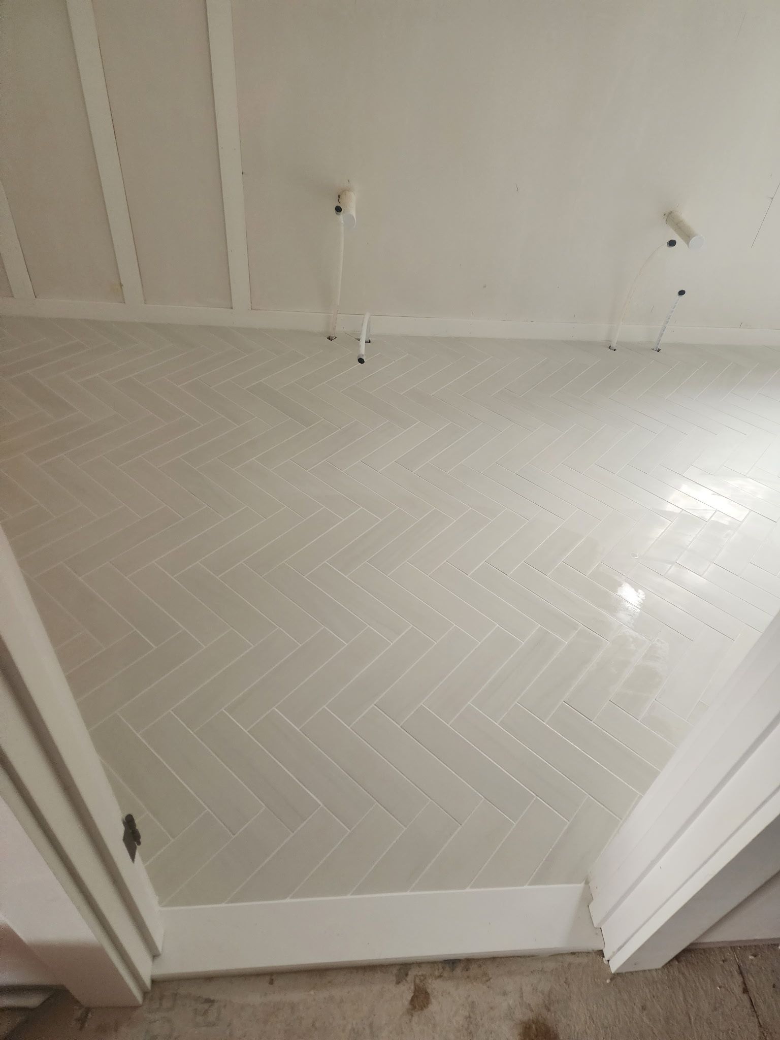 Herringbone pattern tile floor in a white room, viewed from a doorway.