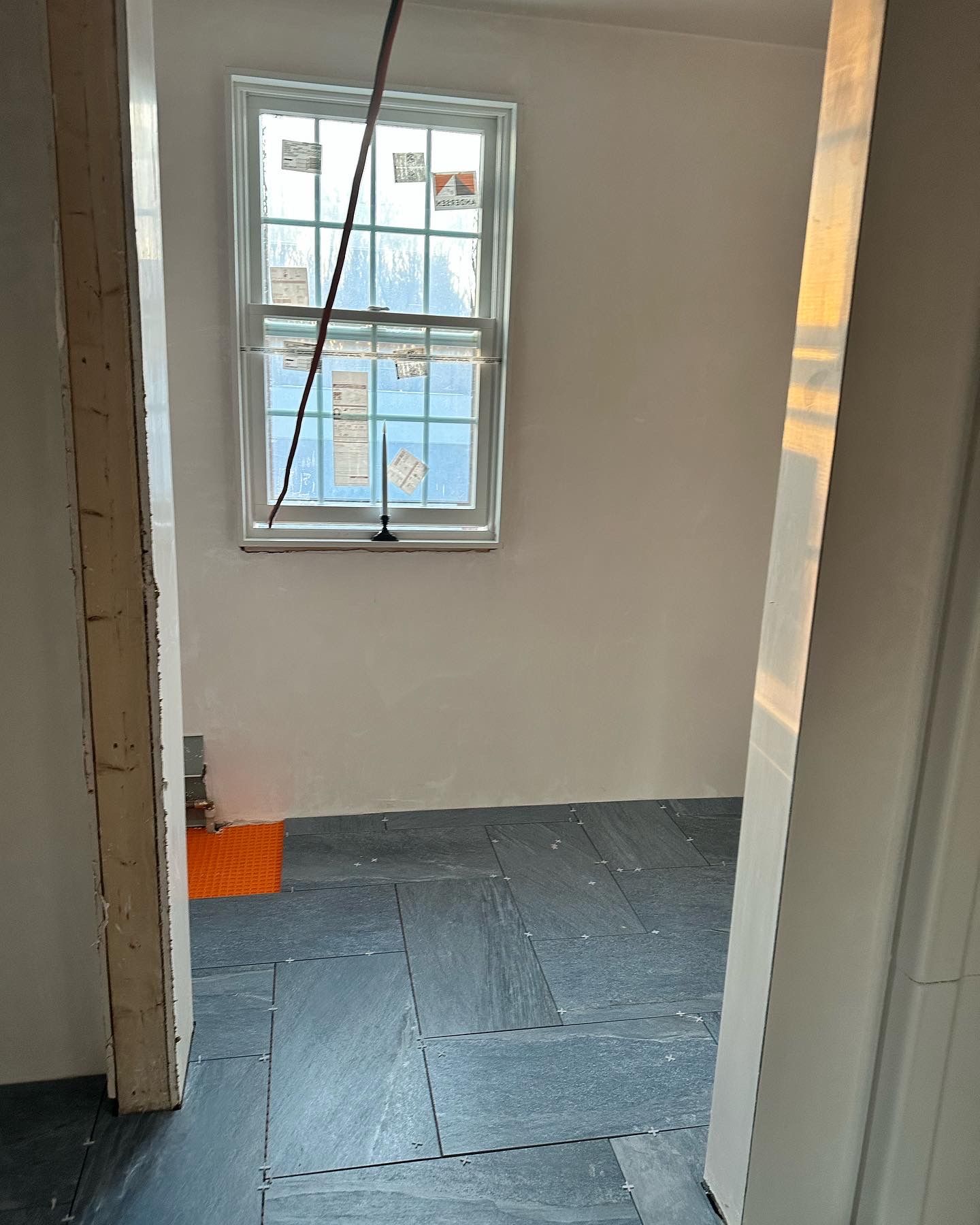 Interior construction view of a room with a window, white walls, and dark flooring.
