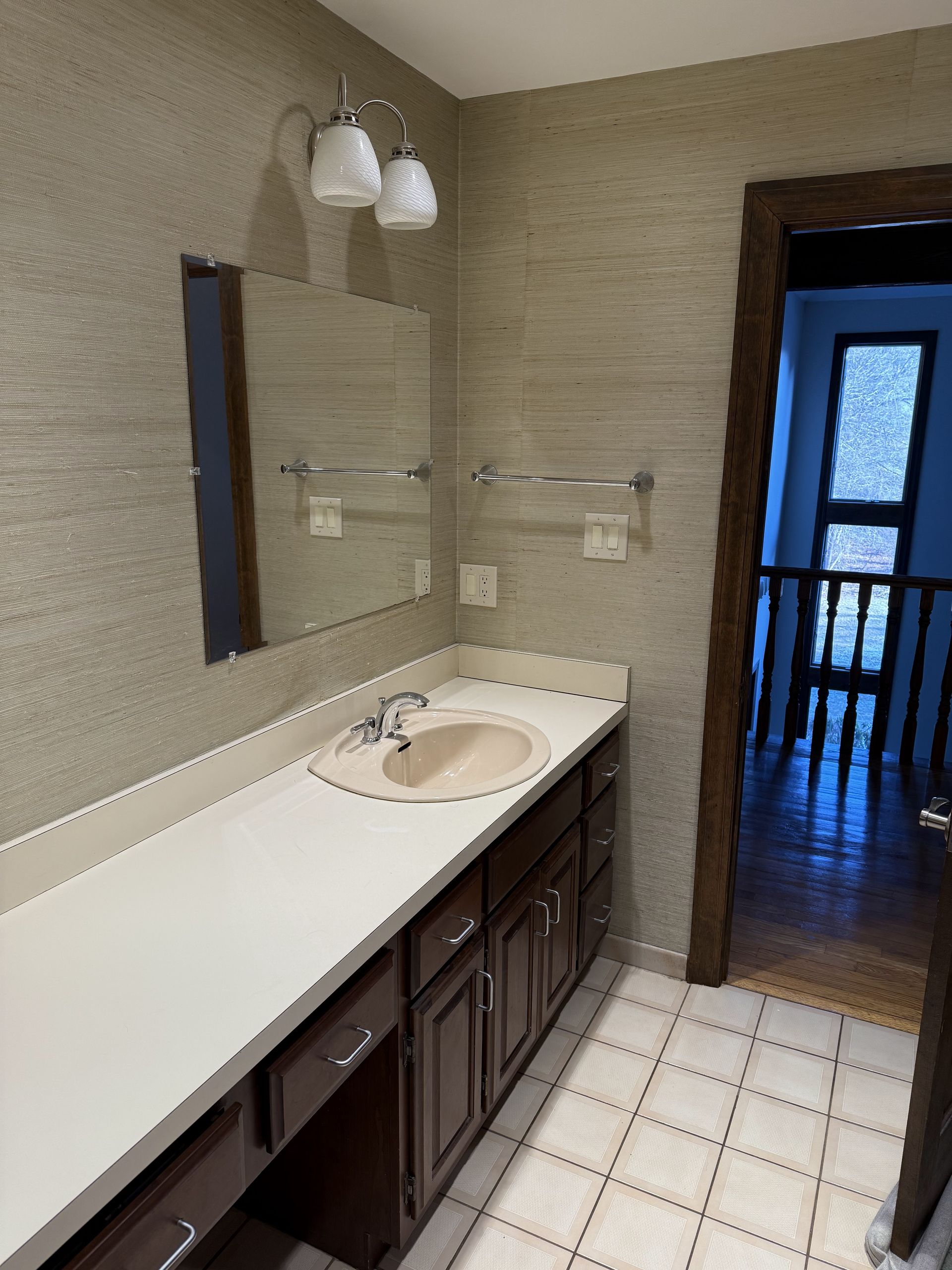 Bathroom with a brown vanity, white countertop, tan walls, and a doorway to another room.