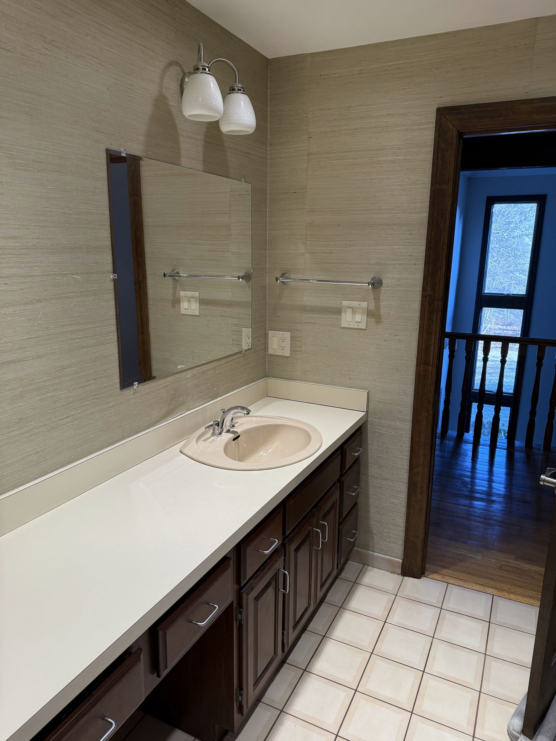 Bathroom with long countertop, mirror, and dark brown cabinets. View into adjacent room.