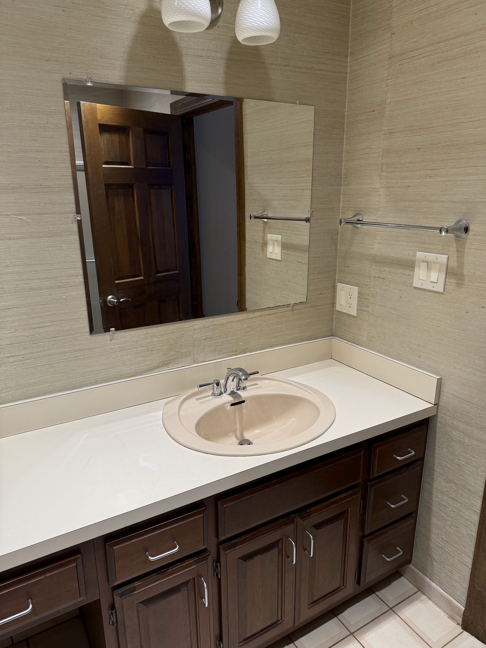Bathroom with dark wood vanity, light-colored countertop, and a beige sink. Mirror and wall-mounted towel rack.