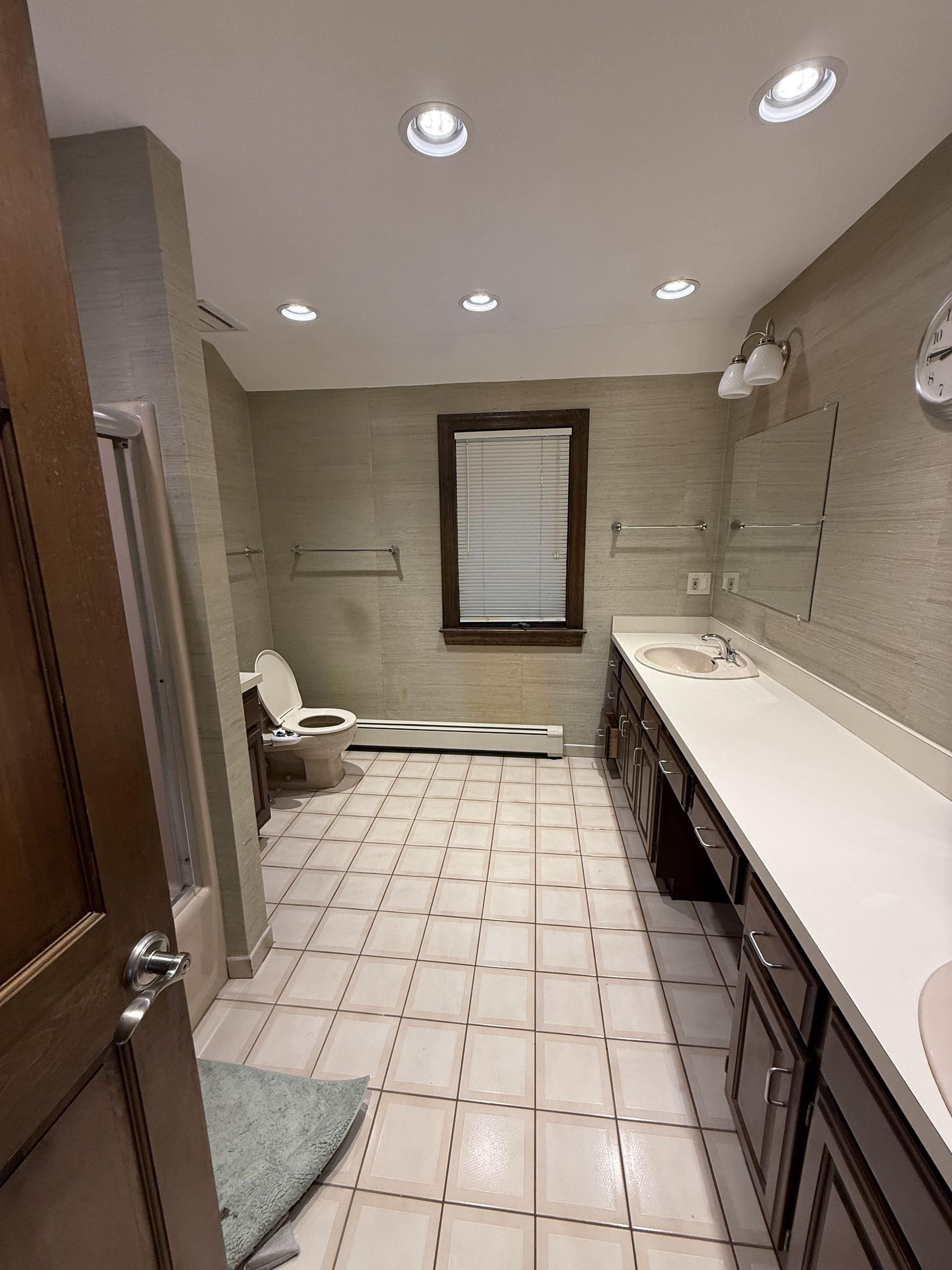 Bathroom with toilet, vanity, and window. Beige tile floor and textured walls.