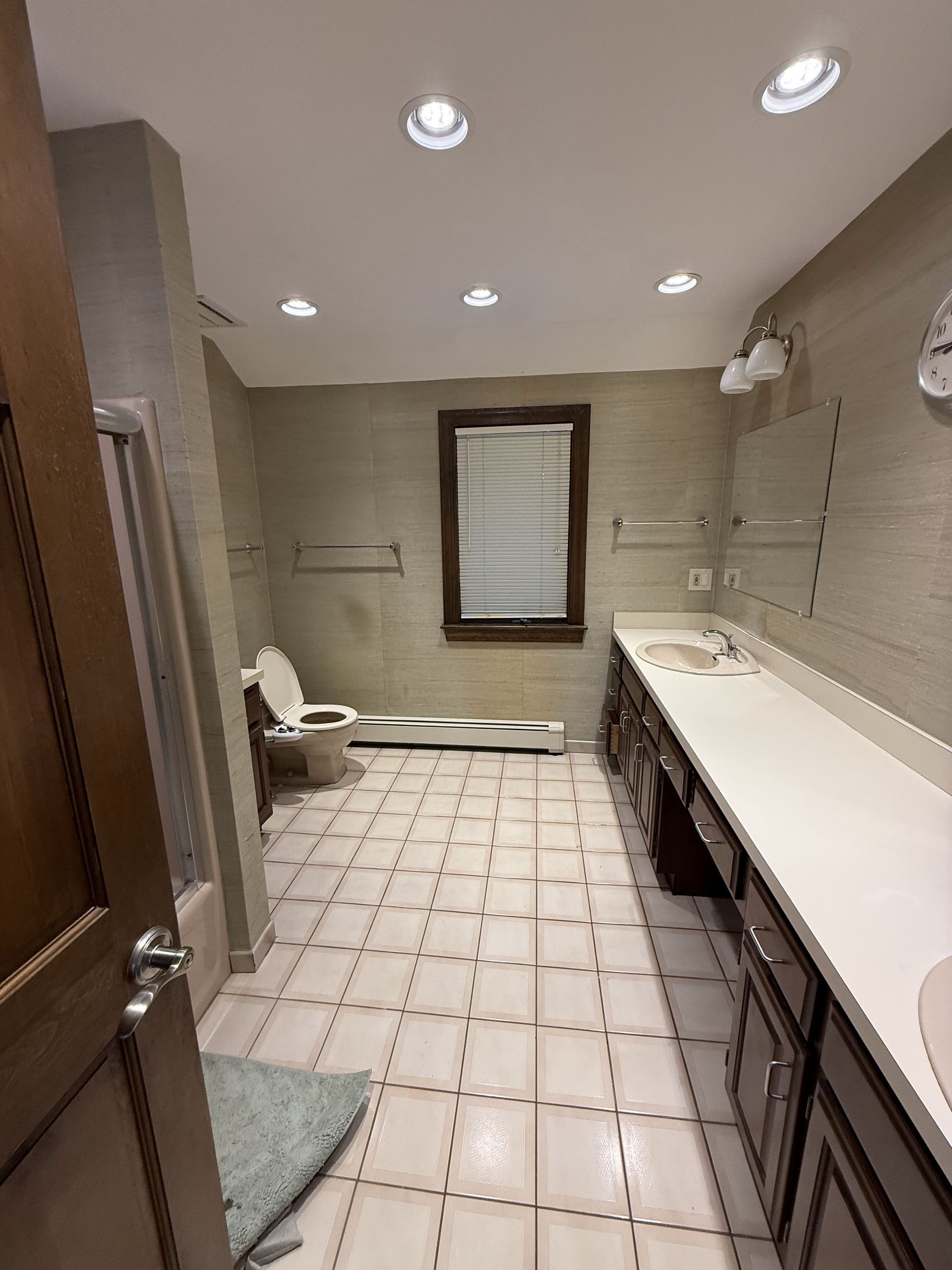 Bathroom with a toilet, vanity, and shower. Tan walls, white countertops, and tile flooring.