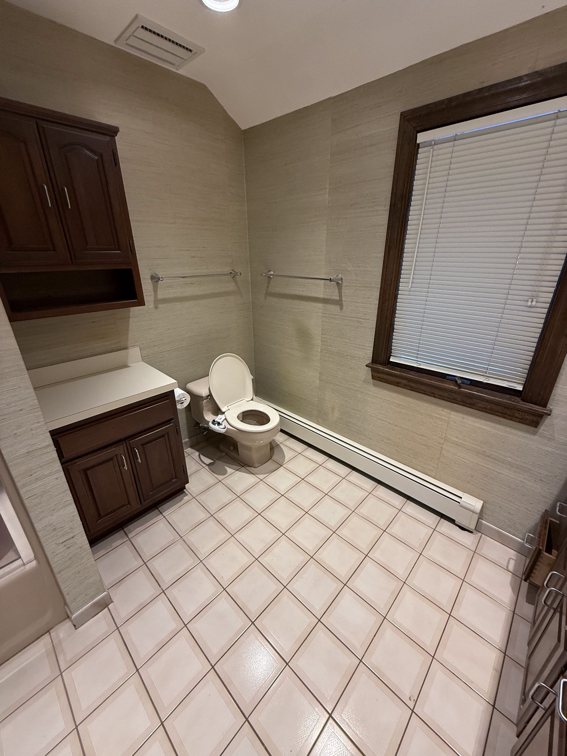Bathroom with tile floor, toilet, vanity, and window. Dark wood cabinets. Beige walls and white blinds.
