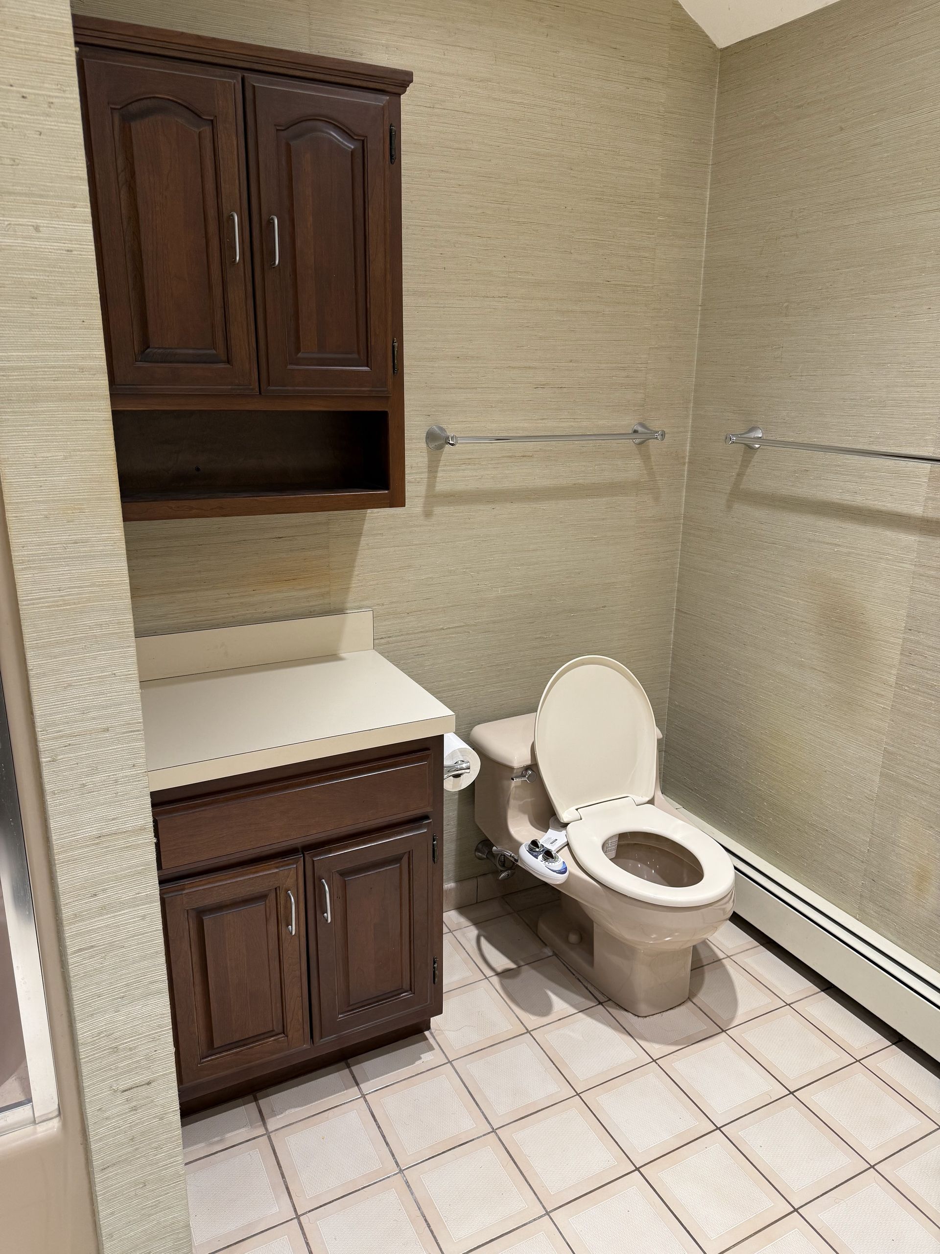 Bathroom with brown cabinets, toilet, and beige patterned wallpaper.