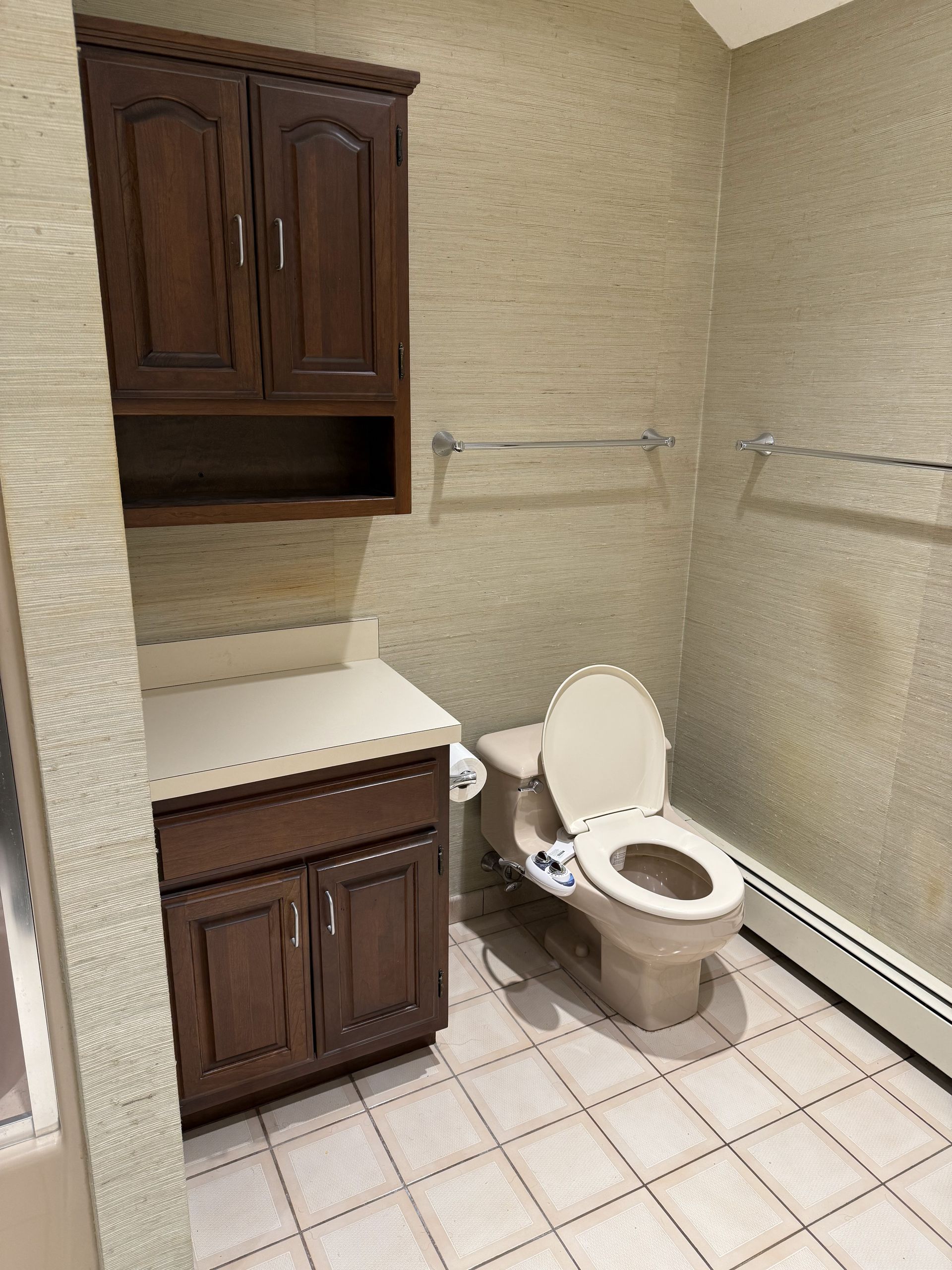 Small bathroom with dark brown cabinets, a toilet, and light-colored wallpaper and floor tiles.