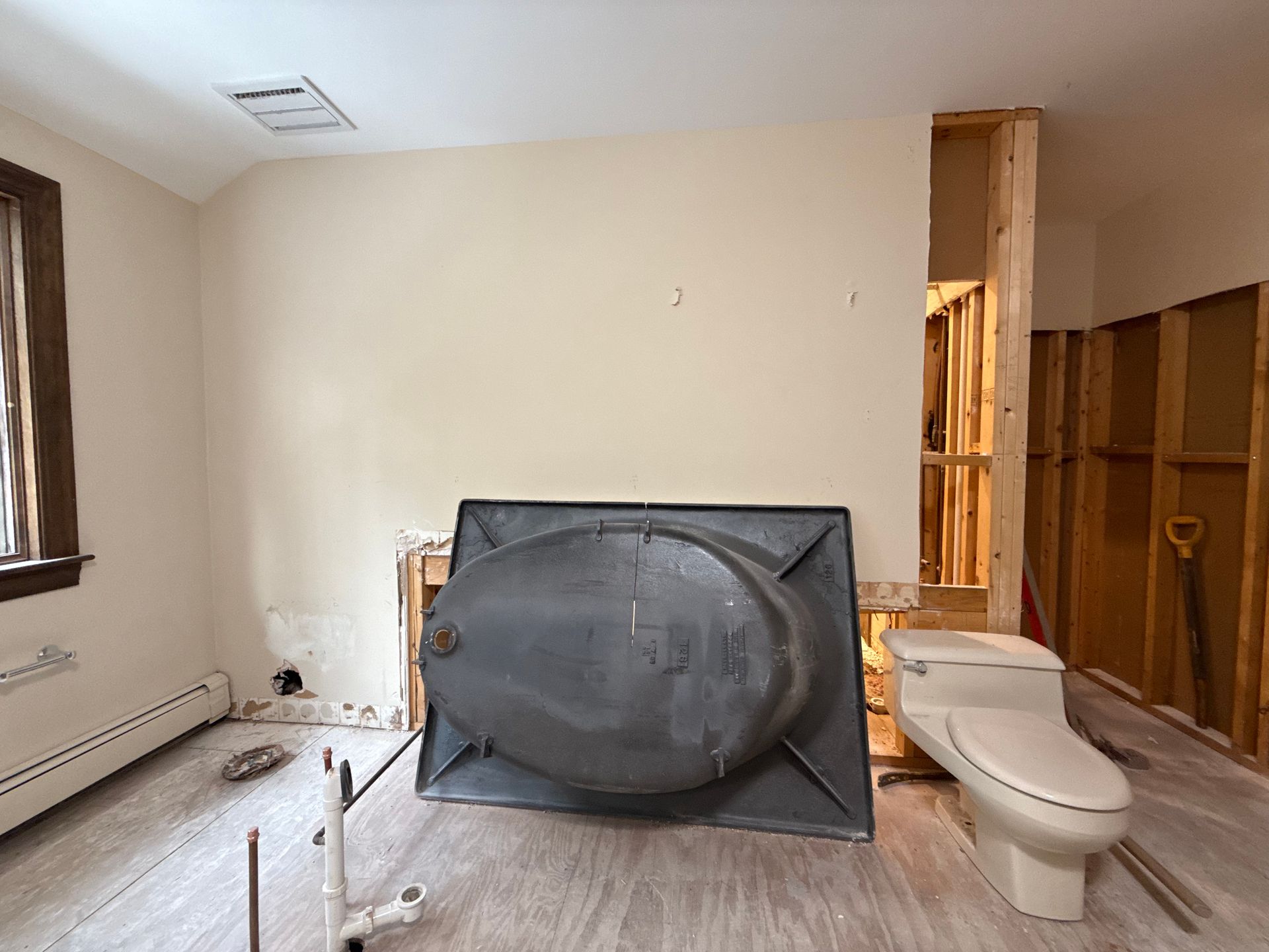 Bathroom remodel in progress; old bathtub sits in front of a wall, toilet nearby.