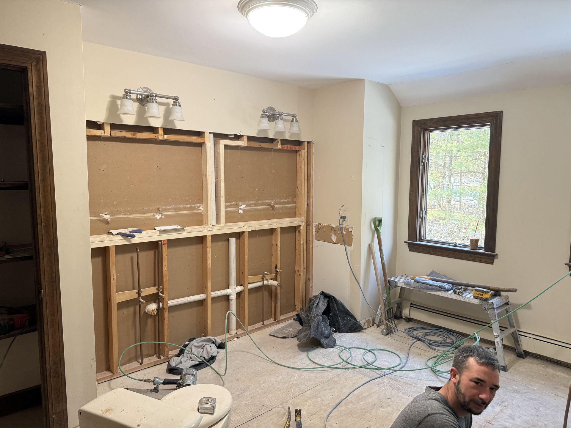 Bathroom renovation in progress. Walls torn open, exposed studs. A man looks at the camera.