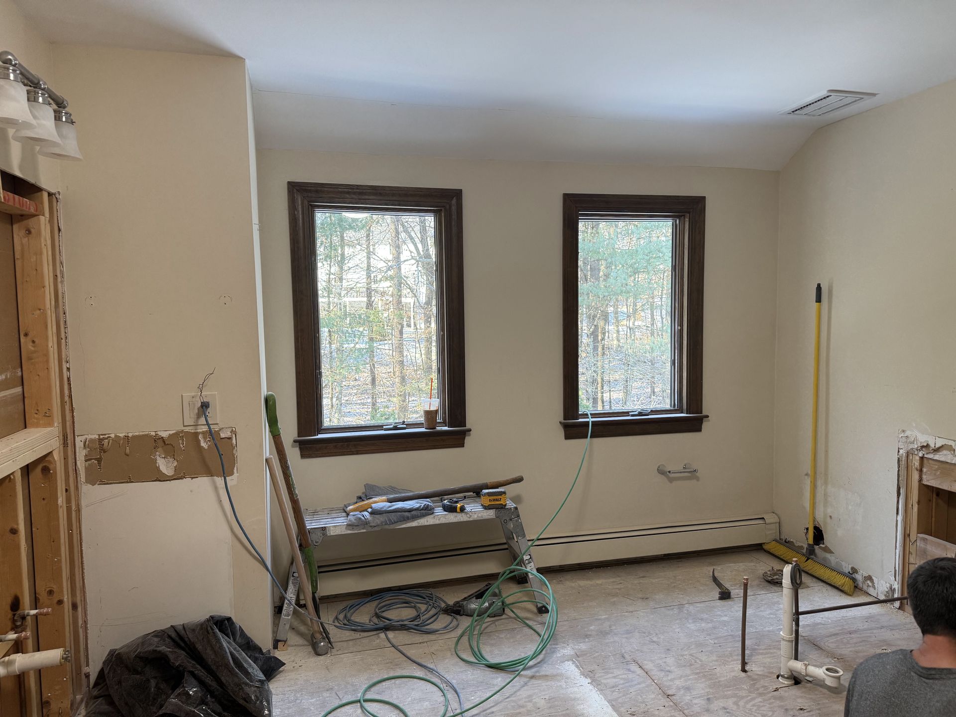 Room under renovation; two windows, exposed wiring, tools, light beige walls, brown window frames, and debris on the floor.